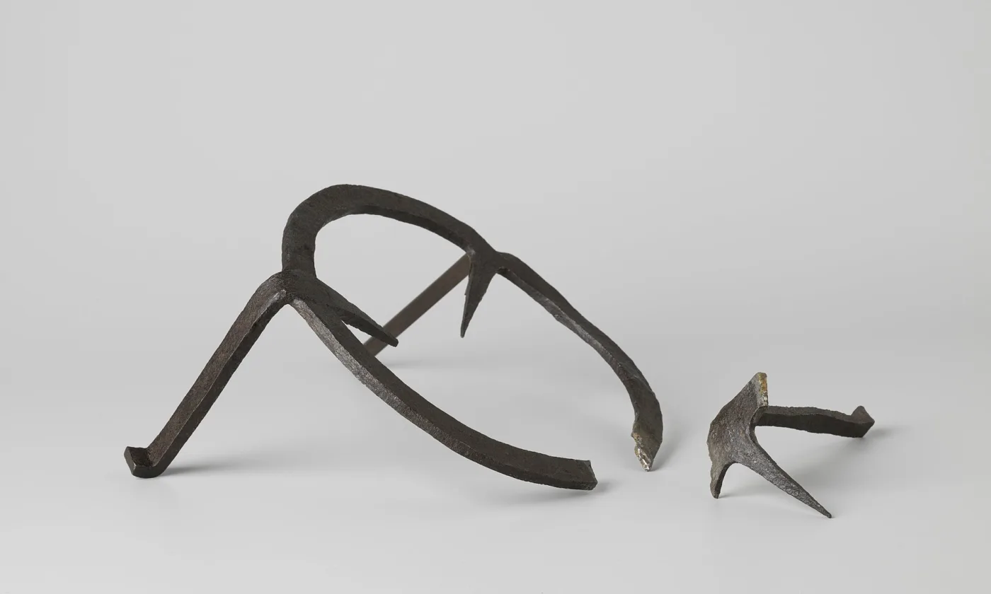 Forged iron ring trivet with three tapering legs bent downwards, lying beside a smaller three-pointed iron fragment