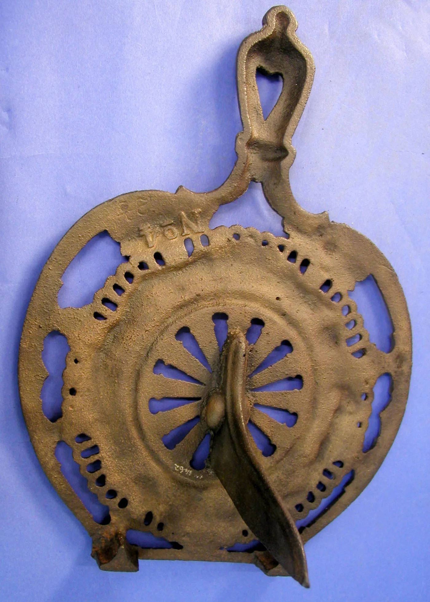 The same trivet from beneath, showing a raised cast number, a long tapering central spike and two short feet at the lower edge