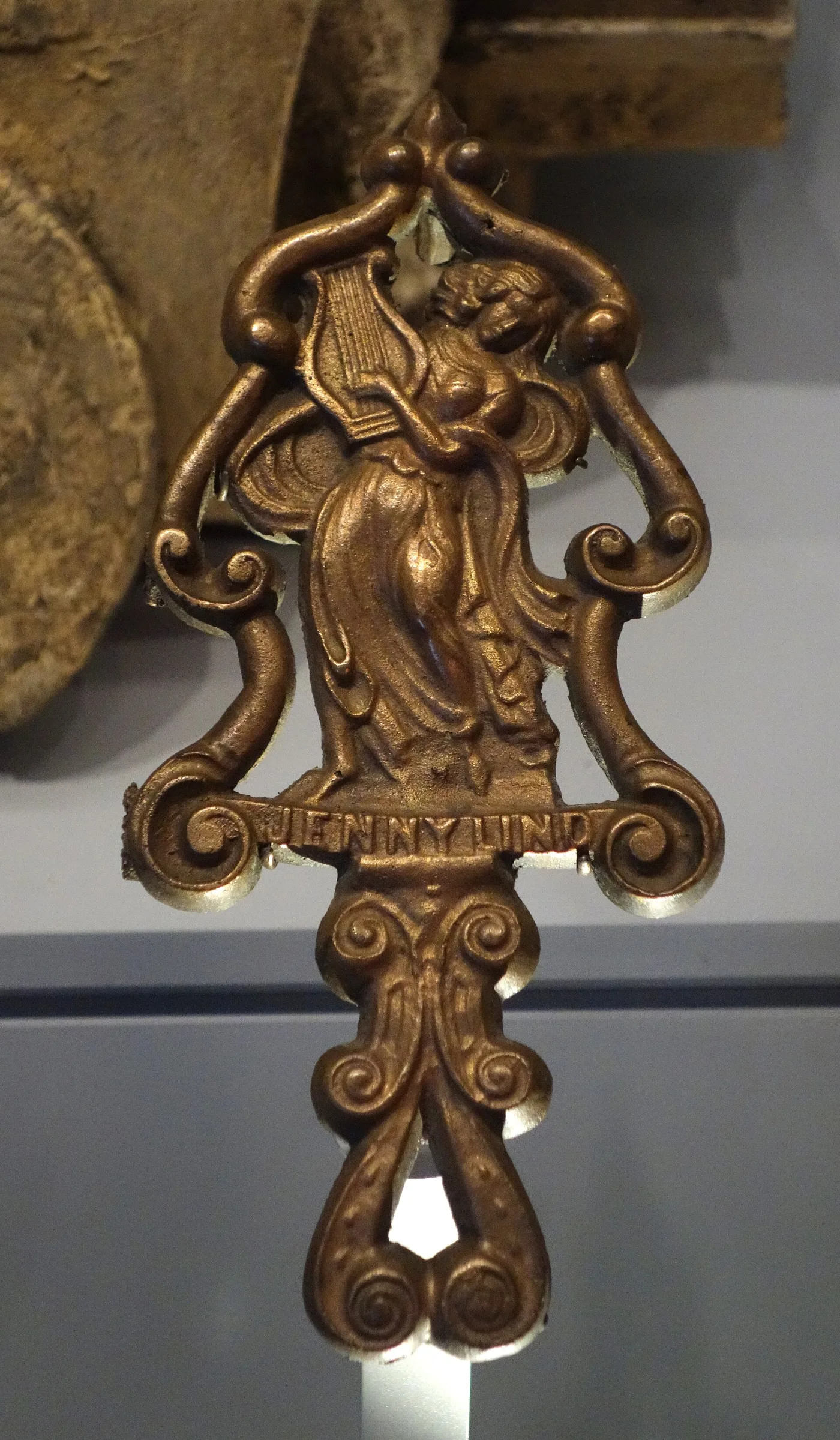 Cast iron trivet handle in the form of a woman in a flowing gown holding a lyre, with the name JENNY LIND cast into a scrolled banner beneath her