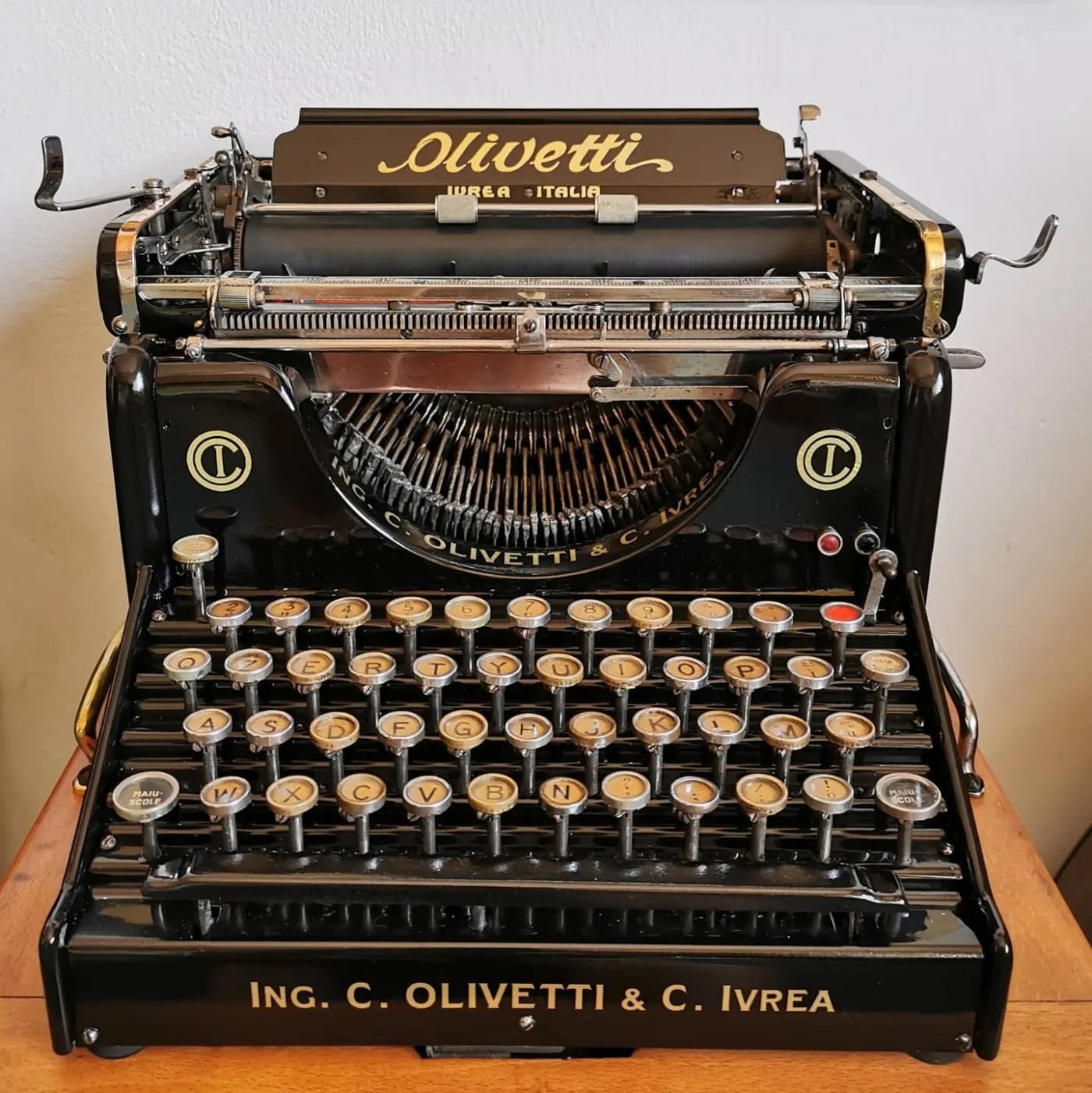Black Olivetti typewriter of 1916 with gold lettering across the paper table, four banks of round keys with white legends under glass, and the maker's name cast across the front rail