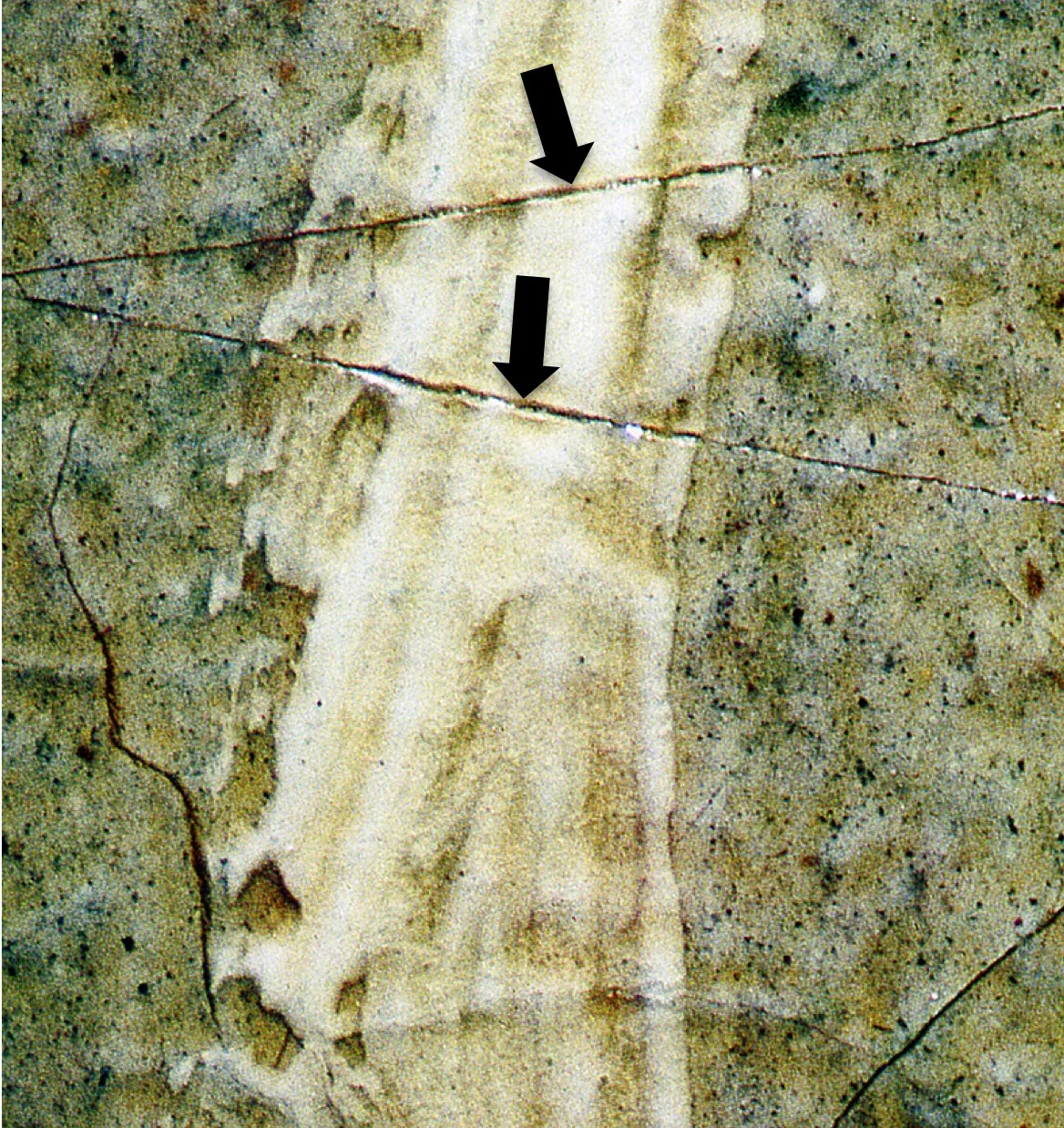 Macro detail of a painted surface with two black arrows marking cracks that were scored into a band of white overpaint
