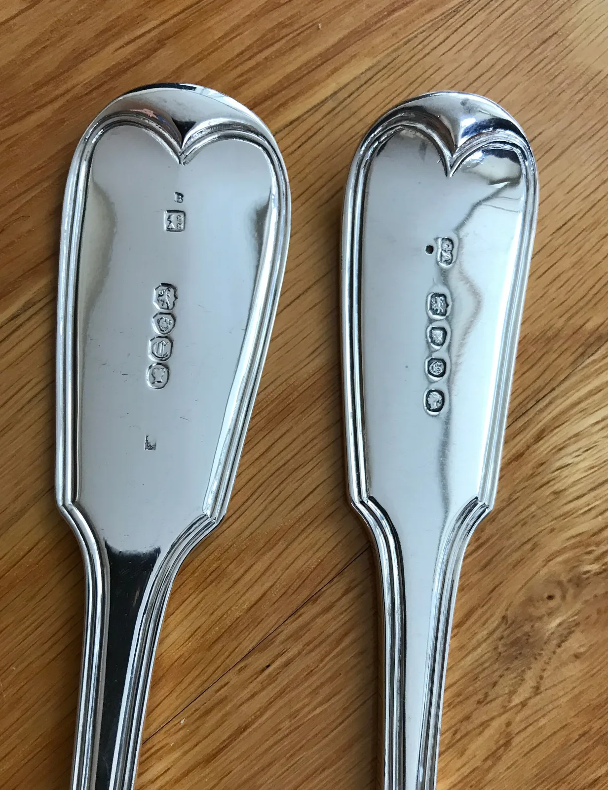 Backs of two English silver spoon handles side by side, each struck with a vertical row of hallmarks plus one small extra mark