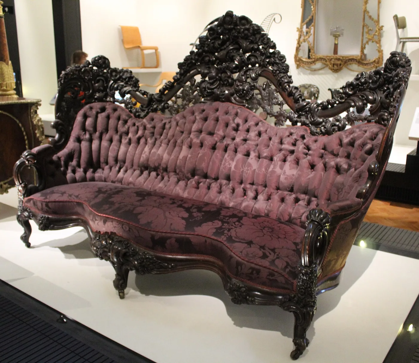 Deeply carved dark rosewood sofa with a pierced crest of grapes, roses and scrolls above a serpentine buttoned back in faded pink silk damask, on cabriole legs with casters