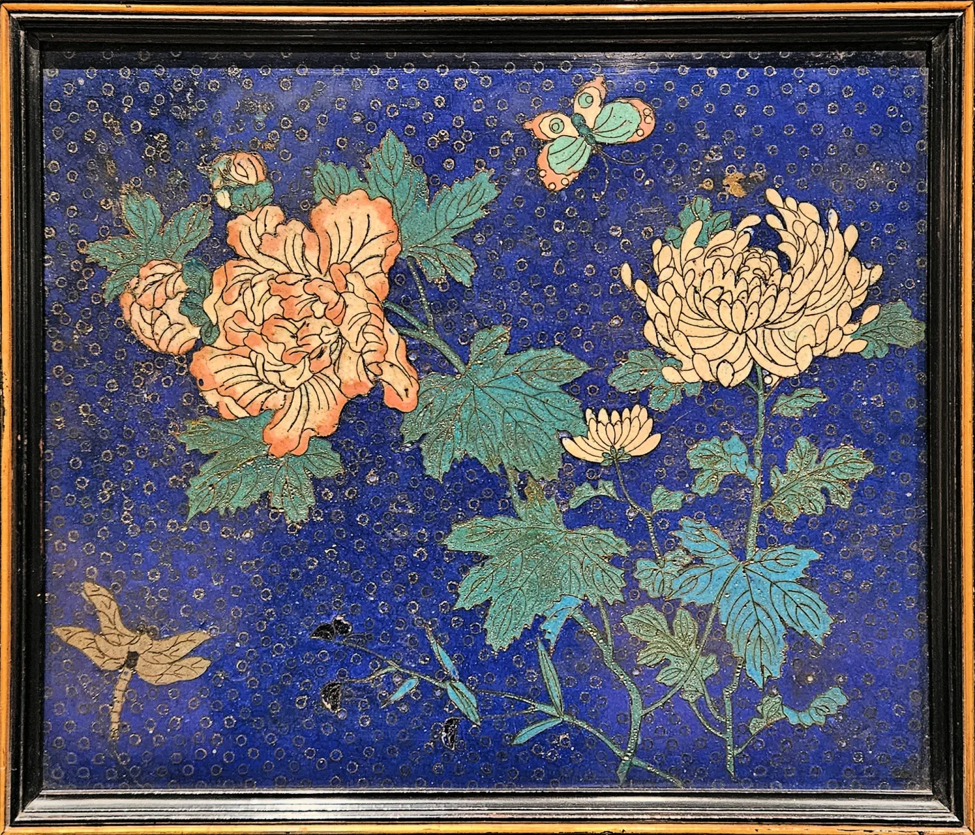Close view of an enamel panel: chrysanthemums, peonies and maple leaves with a butterfly and a dragonfly, on a deep blue ground textured with small rings