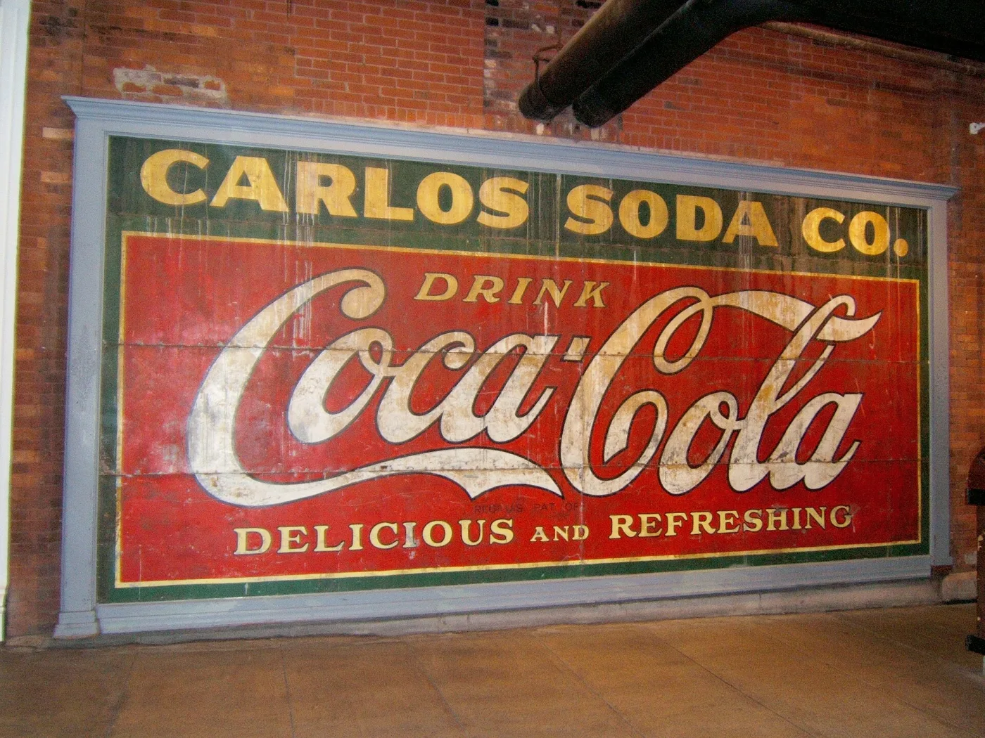 Painted brick wall advertisement in strong red and white reading Carlos Soda Co, Drink Coca-Cola, Delicious and Refreshing, its lettering sharp and its colours unfaded
