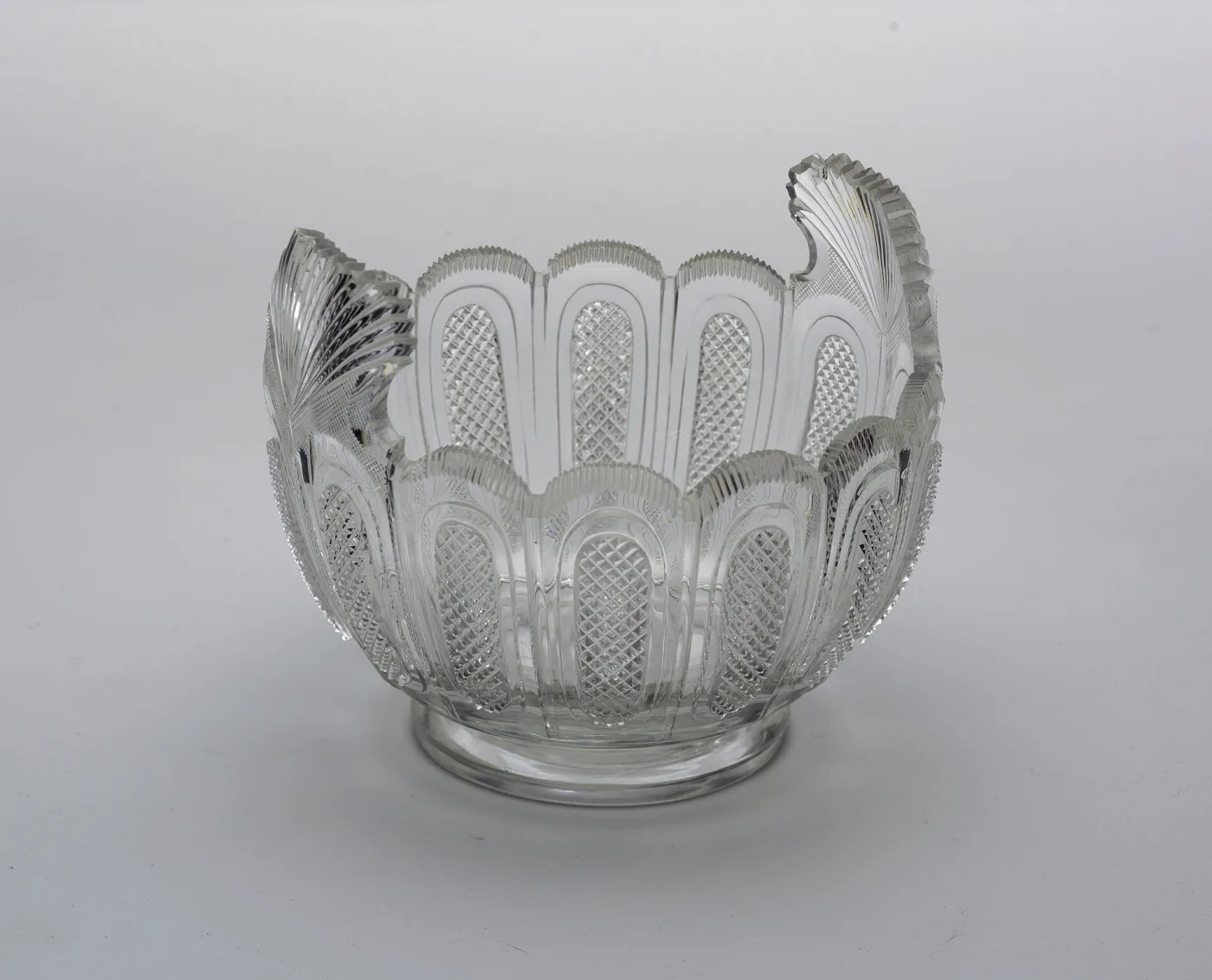 Cut glass bowl with a scalloped serrated rim and two upswept fan-cut handles, the body divided into arched panels of fine diamonds