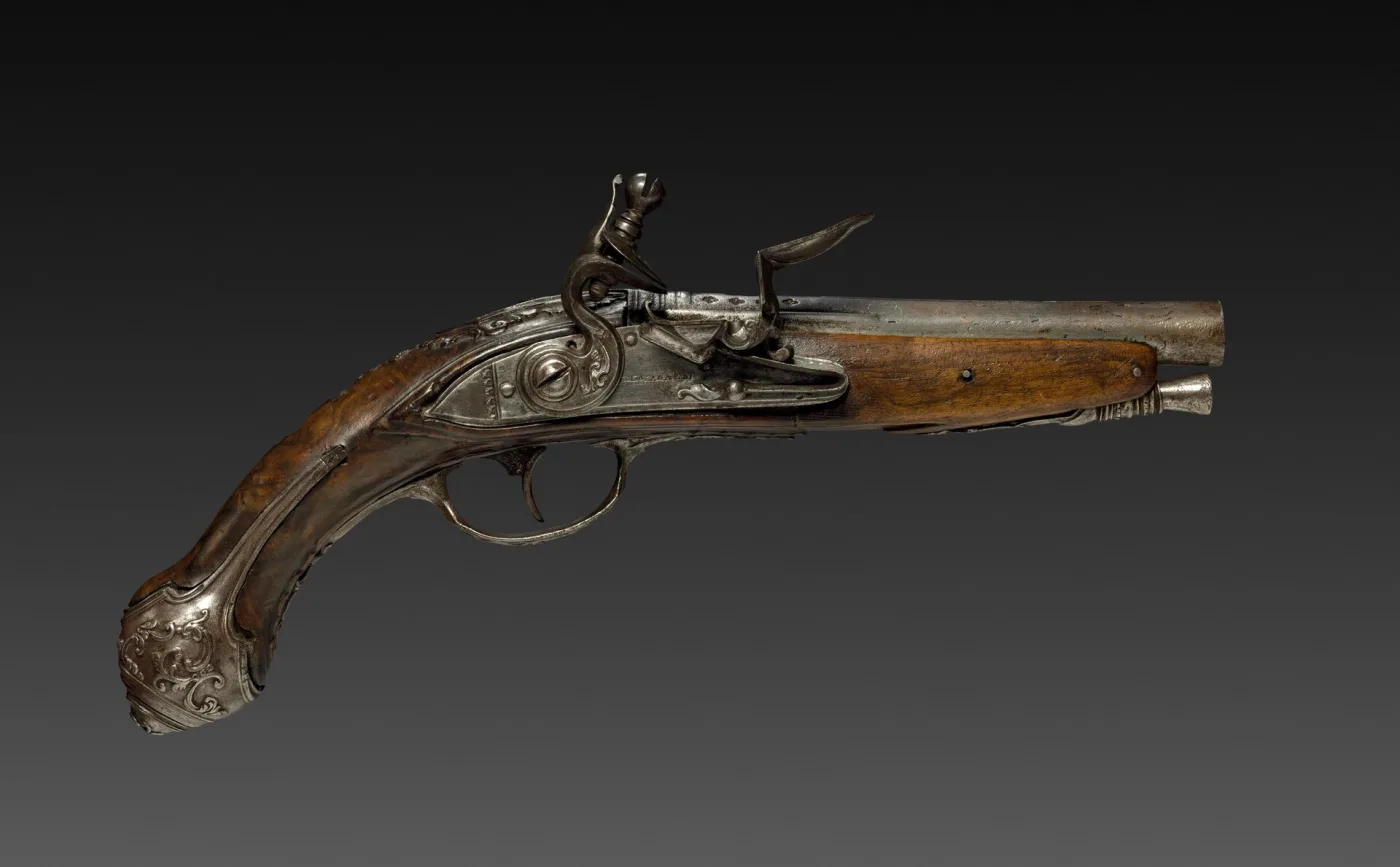 Eighteenth-century flintlock pistol photographed against black, its slender steel barrel running the length of the frame, with a chiselled lock, a walnut stock and a silver-mounted butt cap
