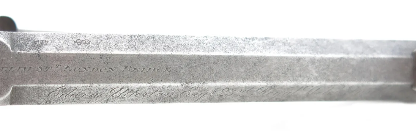 Close view along the flat top of a revolver barrel, showing a line of stamped lettering and small proof marks running down the centre of the polished steel