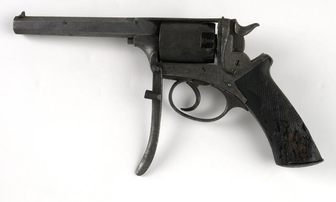 Percussion revolver of the 1850s seen from the side, with an octagonal barrel, a fluted cylinder, an open trigger guard and a chequered wooden grip, the metal worn to a grey patina