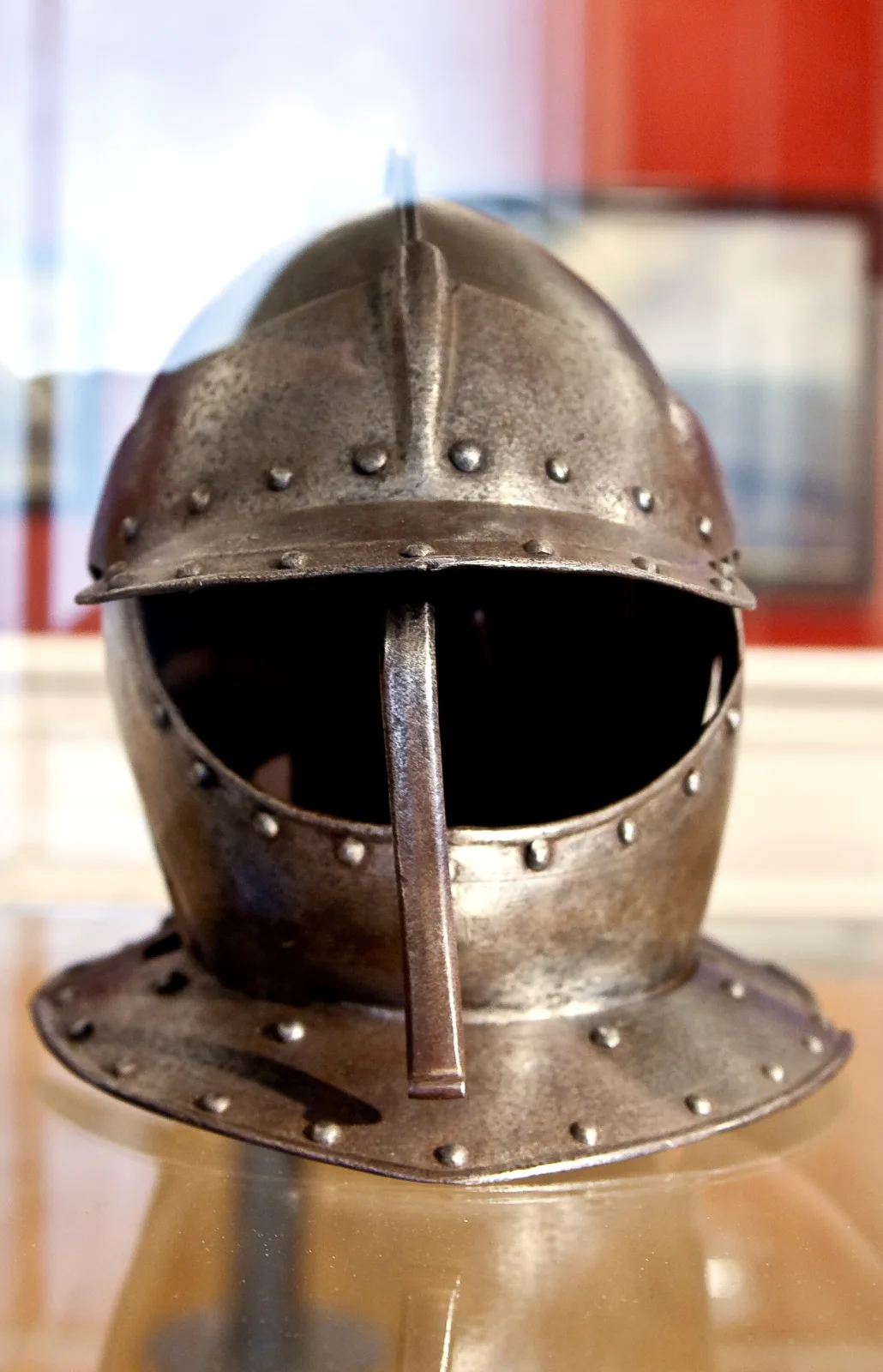 Seventeenth-century cuirassier's helmet in blackened steel with a rounded skull, a raised comb, a pivoting three-bar face guard and a flared neck plate studded with rivets