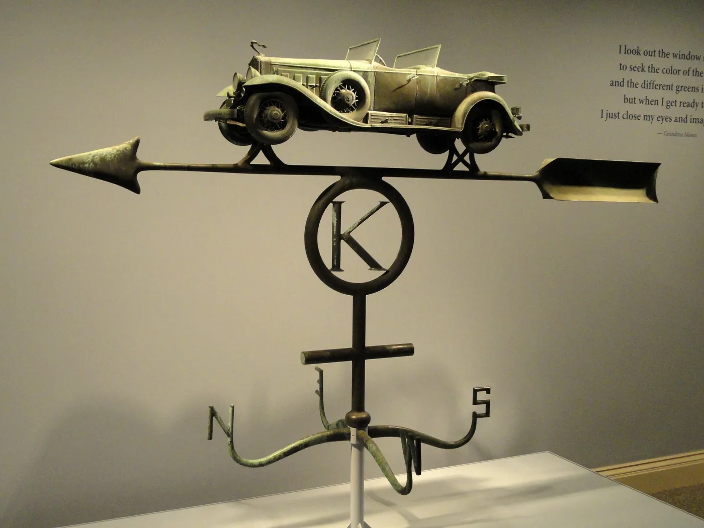 A weathervane in the form of a 1930s Cadillac open-topped touring car, mounted on a directional rod in a museum gallery