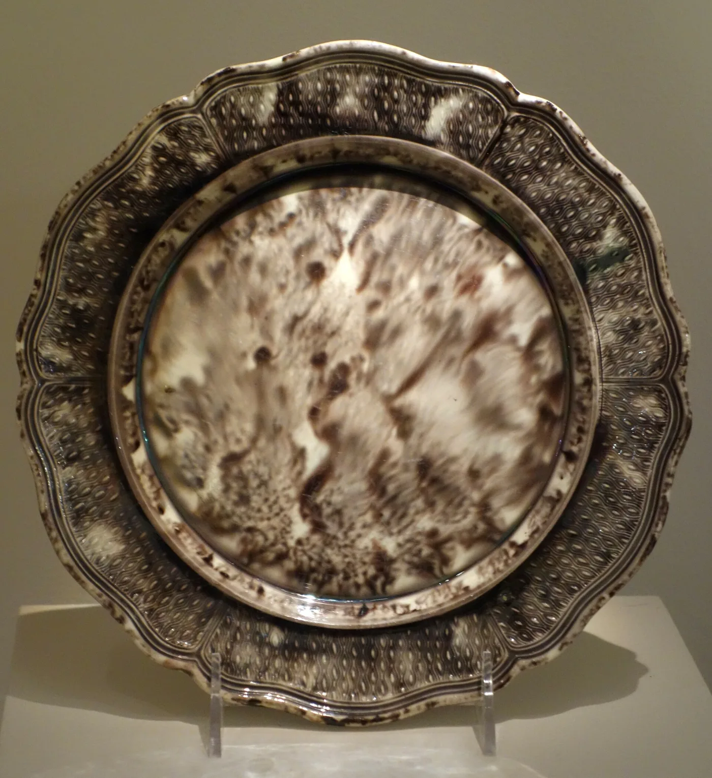 Creamware plate of about 1770 with a scalloped and moulded rim, its whole surface running with mottled brown, grey and cream glaze in the tortoiseshell manner