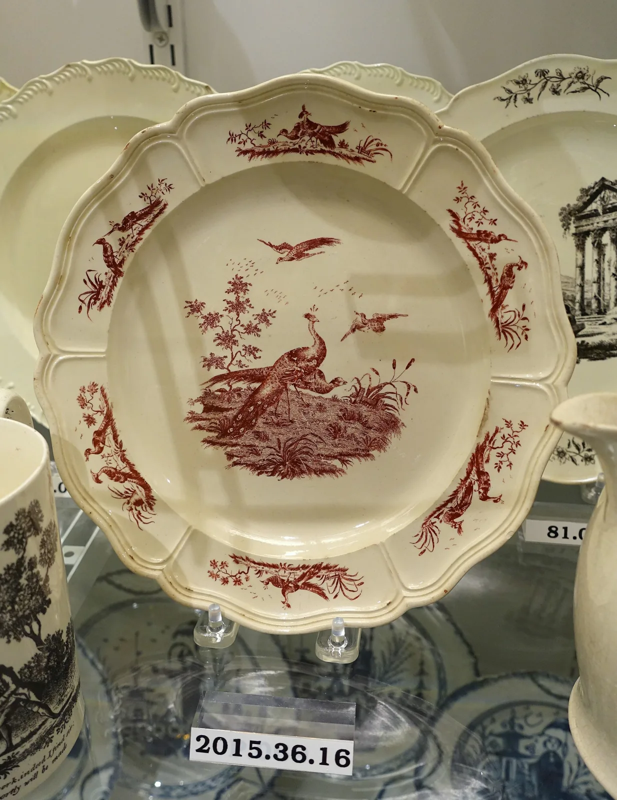 Creamware plate with a moulded scalloped rim, transfer-printed in red with an exotic bird among foliage in the centre and scattered sprigs around it