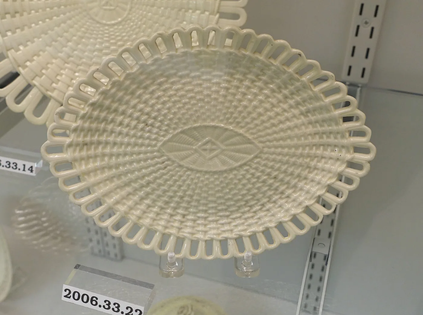 Oval creamware stand with a pierced openwork border of interlocking loops around a plain moulded well, in pale cream, resting on a museum shelf