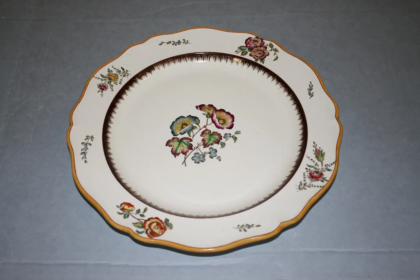 Plate seen from above, its rim moulded and picked out in a narrow brown and gilt band, with a small spray of painted flowers in the centre well