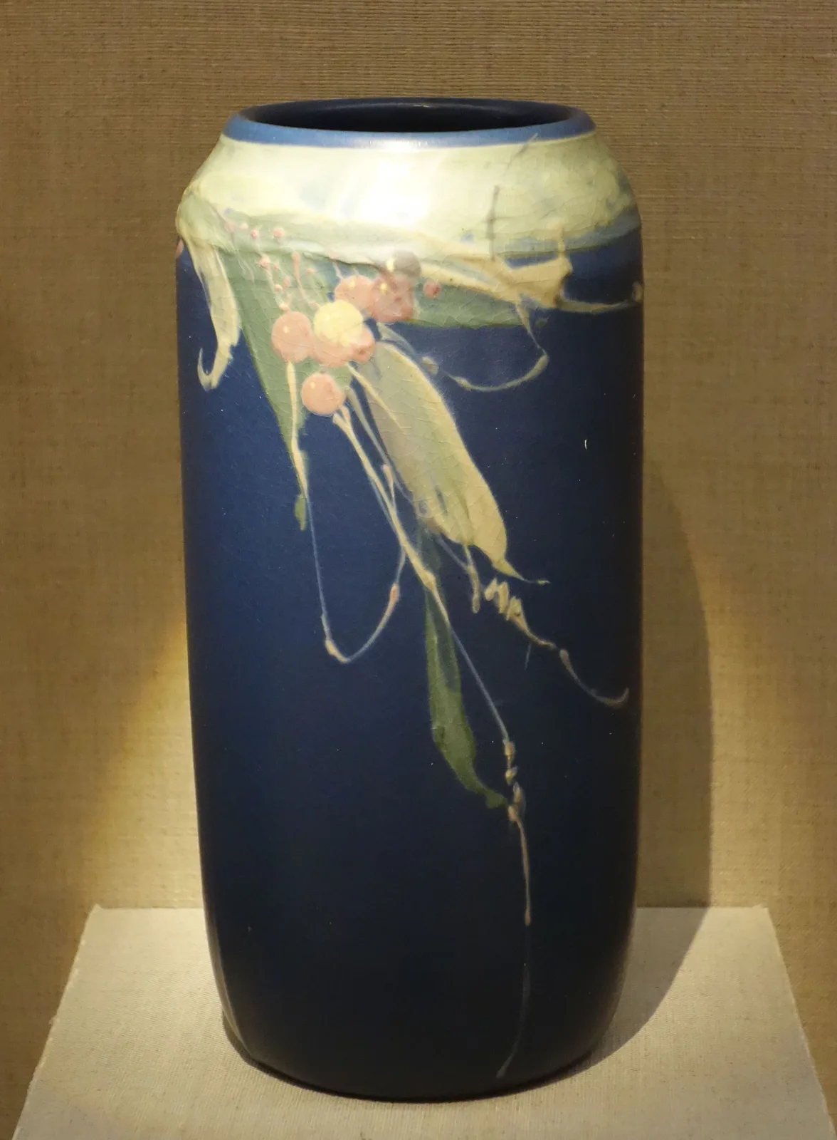 Tall cylindrical vase glazed deep blue-black shading to olive at the shoulder, painted with a branch bearing long leaves and small orange berries under a high gloss