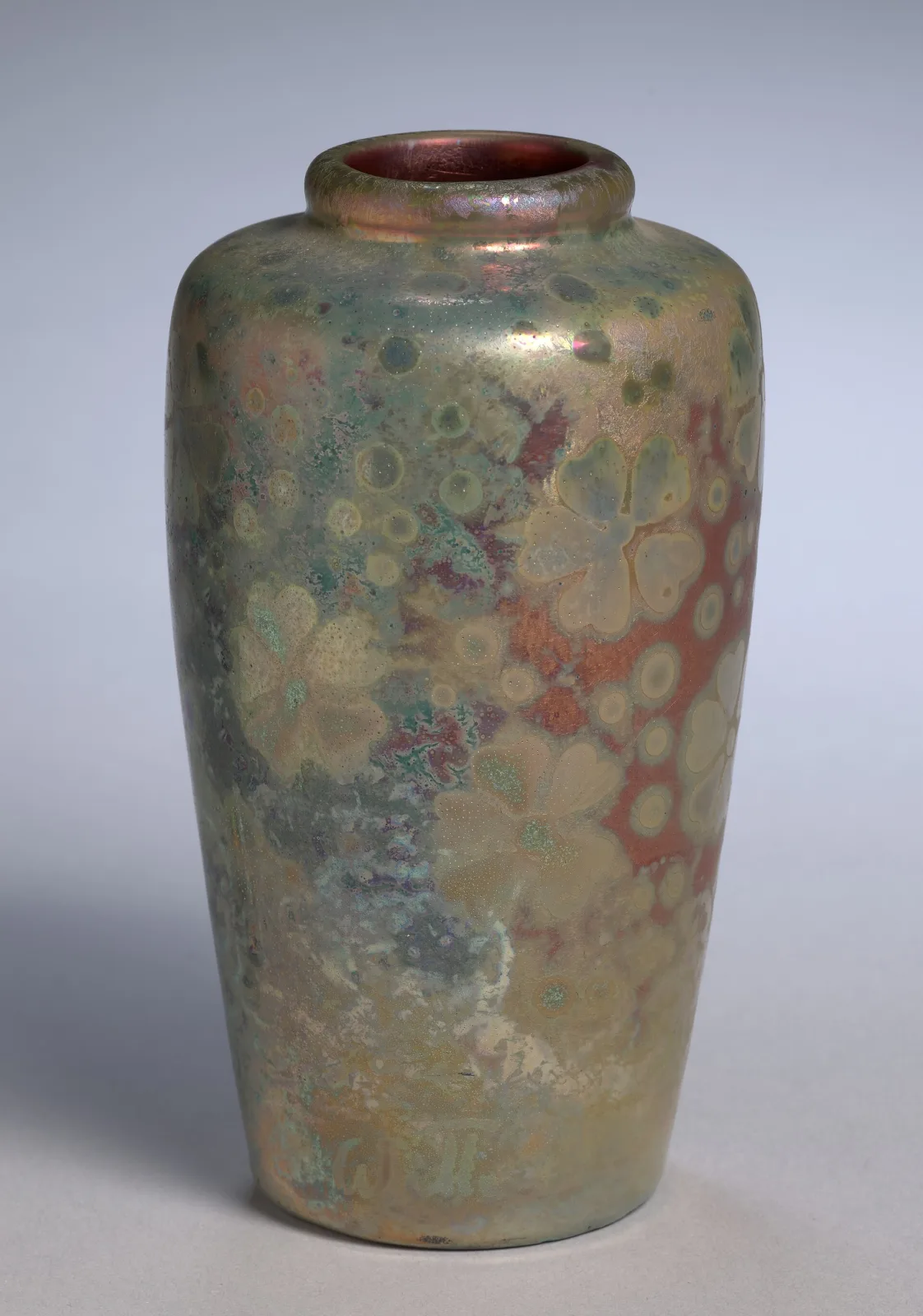Tall tapering vase covered in an iridescent glaze of green, gold and rose, patterned with large open flowers and scattered dots that shimmer against the ground
