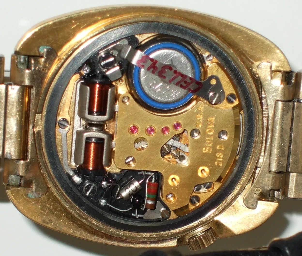 Open gold watch case showing a Bulova tuning fork movement with two copper coils, a battery and a gold plate stamped Bulova 218 D