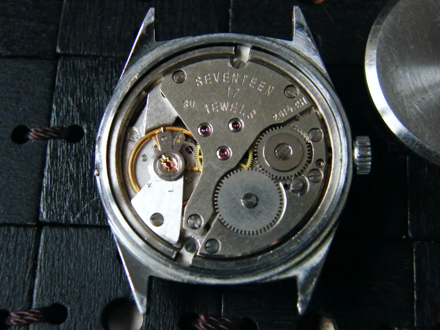 Steel watch case with the back removed, showing a movement stamped Seventeen 17 Jewels and the caliber number 2614.2H
