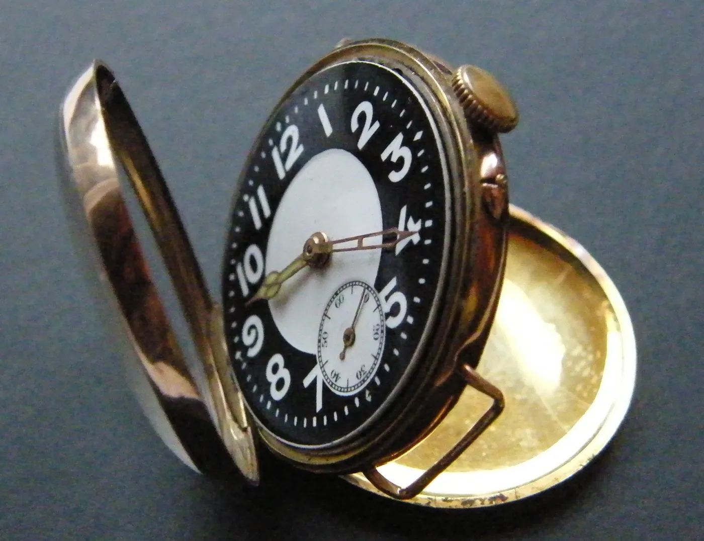 Gold-cased wristwatch of 1916 with its hinged cover swung open, showing a black dial with white luminous numerals
