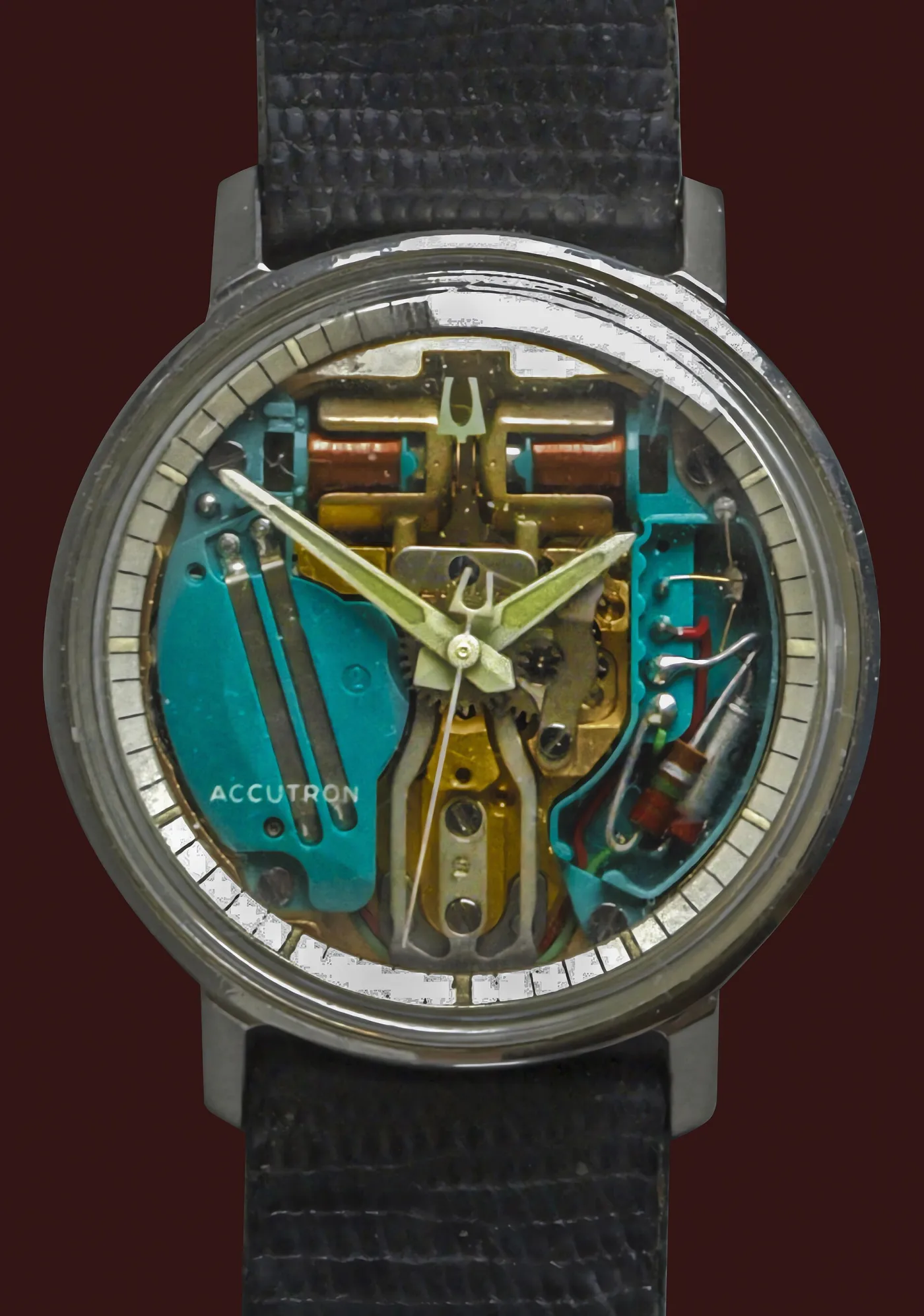 Wristwatch with a transparent dial showing a gold tuning fork, two copper coils and a green circuit plate marked Accutron