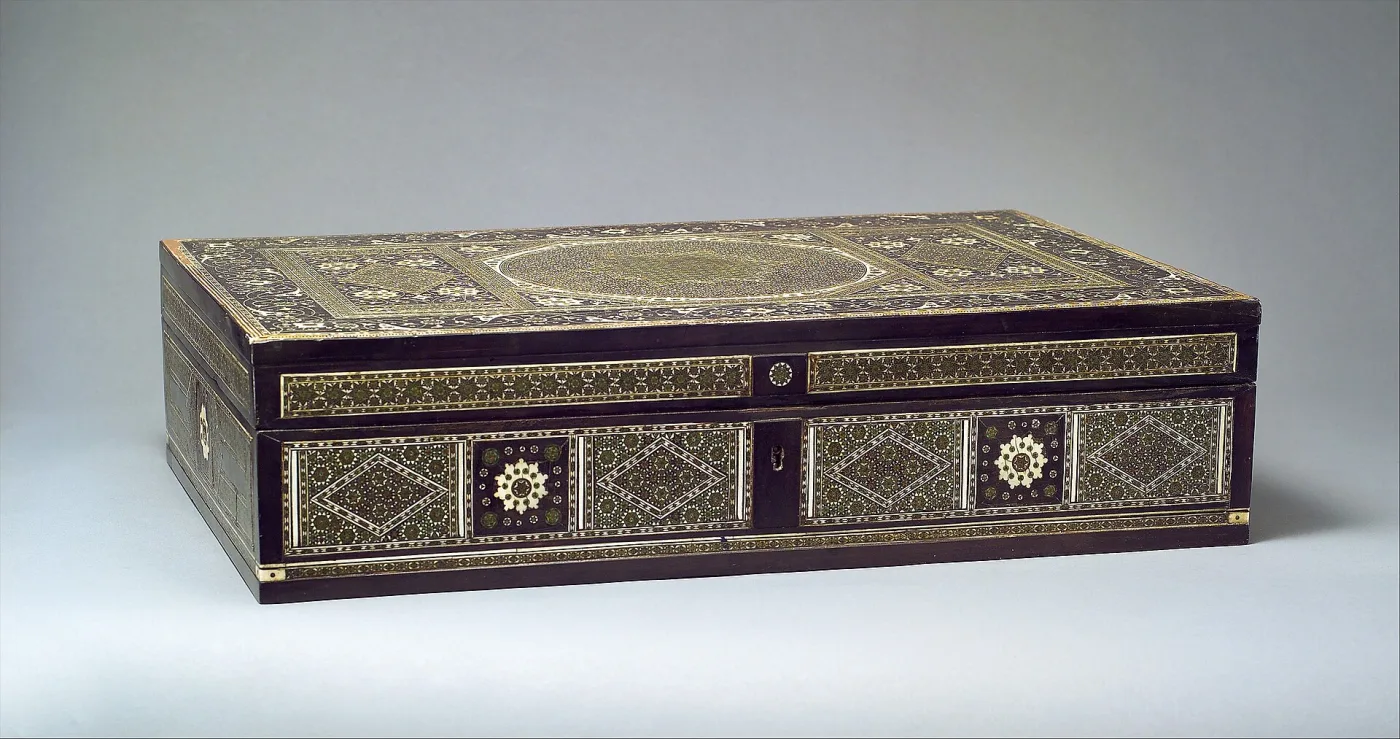 Long low rectangular writing box seen from the front, its whole surface inlaid in geometric bands of pale bone and dark wood, with a small drawer at one end