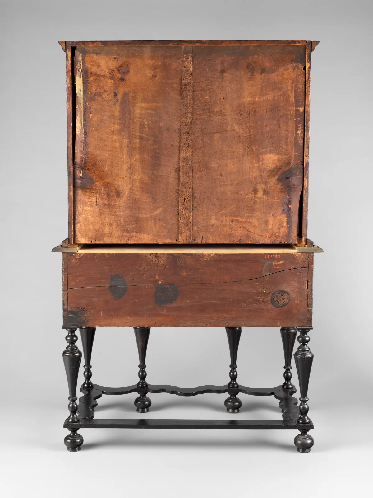 Back of an early eighteenth-century high chest of drawers on turned legs, the upper case made of wide unfinished pine boards darkened to an uneven reddish brown