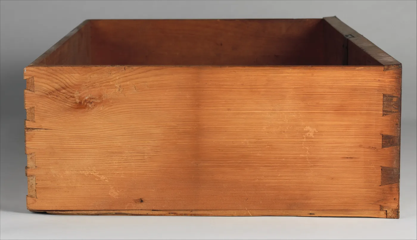 Pine drawer box with hand-cut dovetails at both front corners, its unfinished side toned a warm honey colour with darker streaks at the top edge