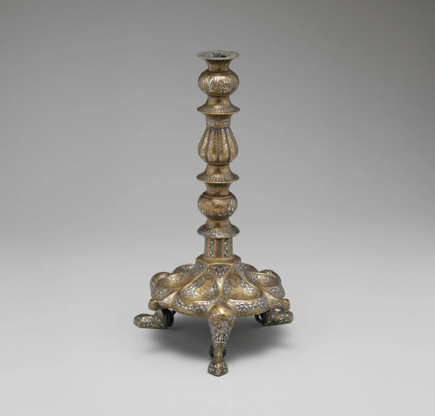 Cast metal candlestick with a knopped baluster stem rising from a pierced, domed tripod base engraved with foliate ornament and standing on three animal-paw feet