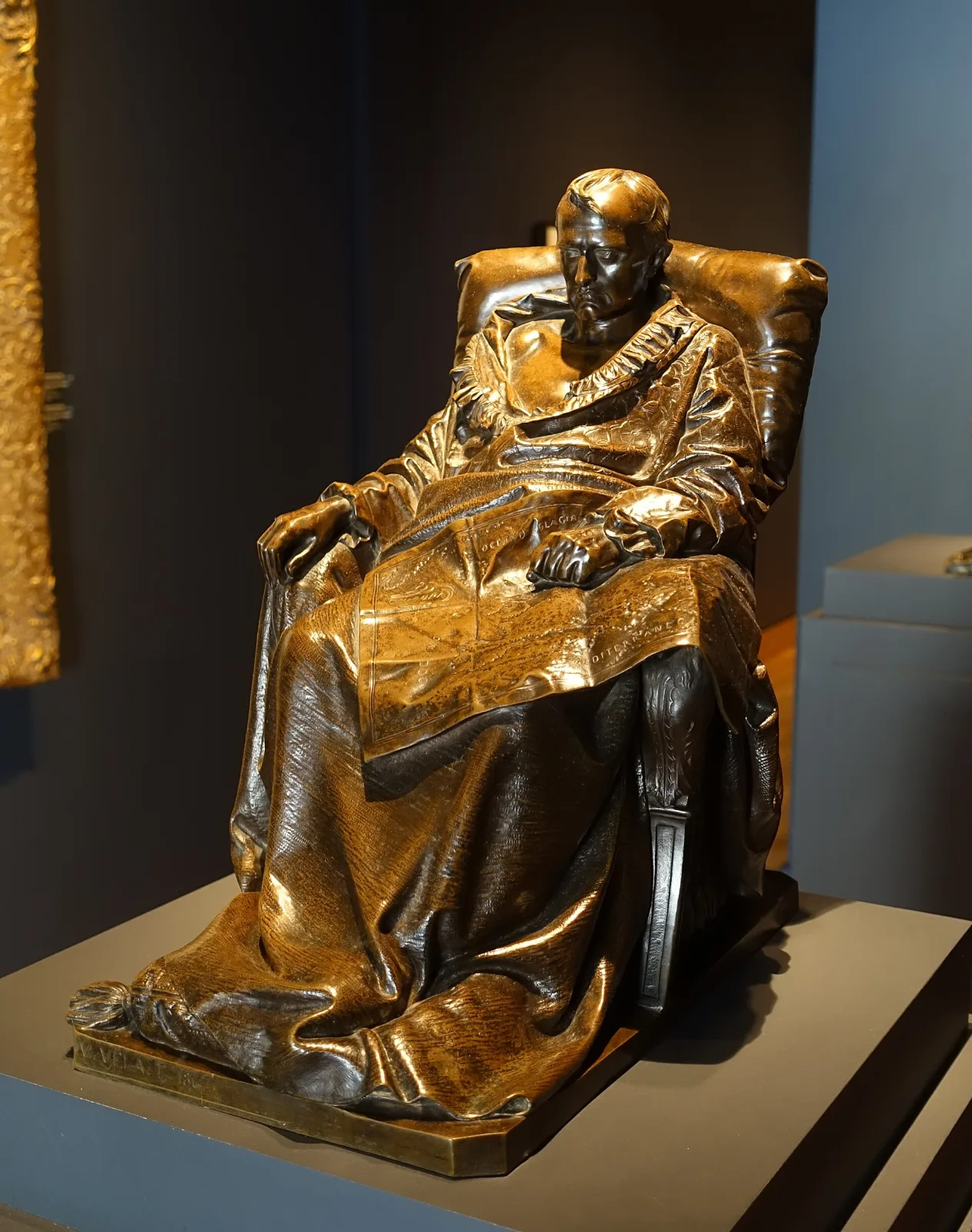Seated bronze figure of Napoleon in a chair, the metal a deep warm brown with lighter tone catching the raised folds of the coat