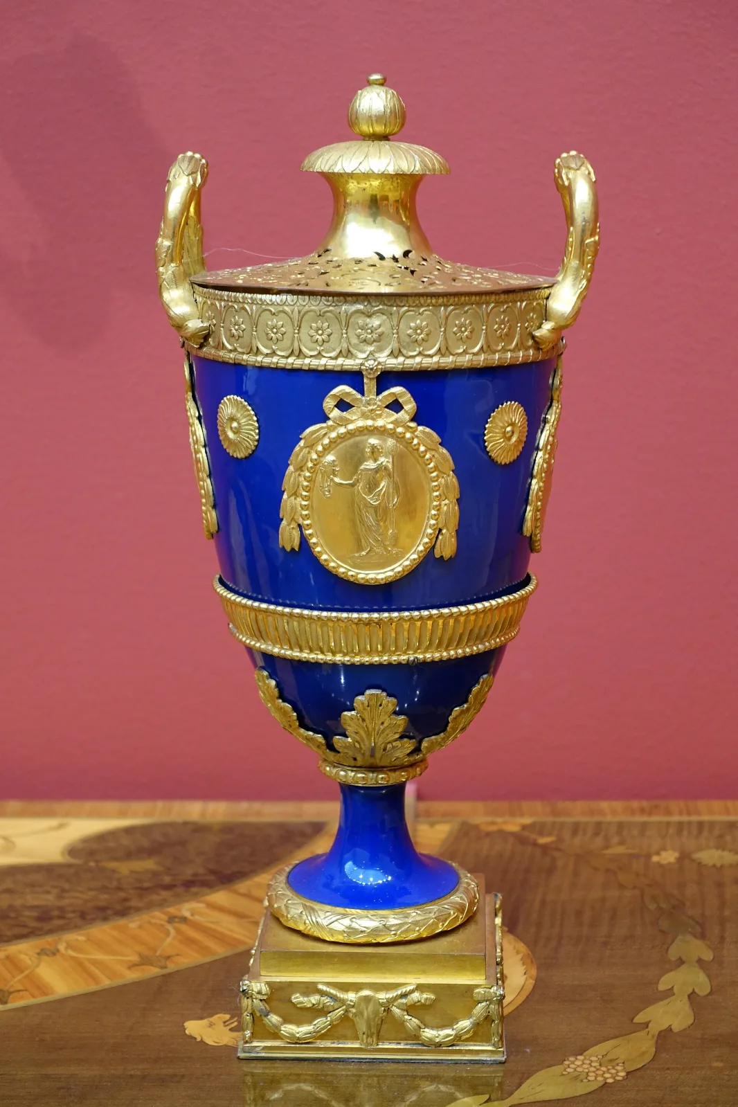 Ovoid urn with a deep blue enamelled body and cover, mounted with gilt bronze handles, rim, foot and an oval medallion, standing on a square gilt plinth