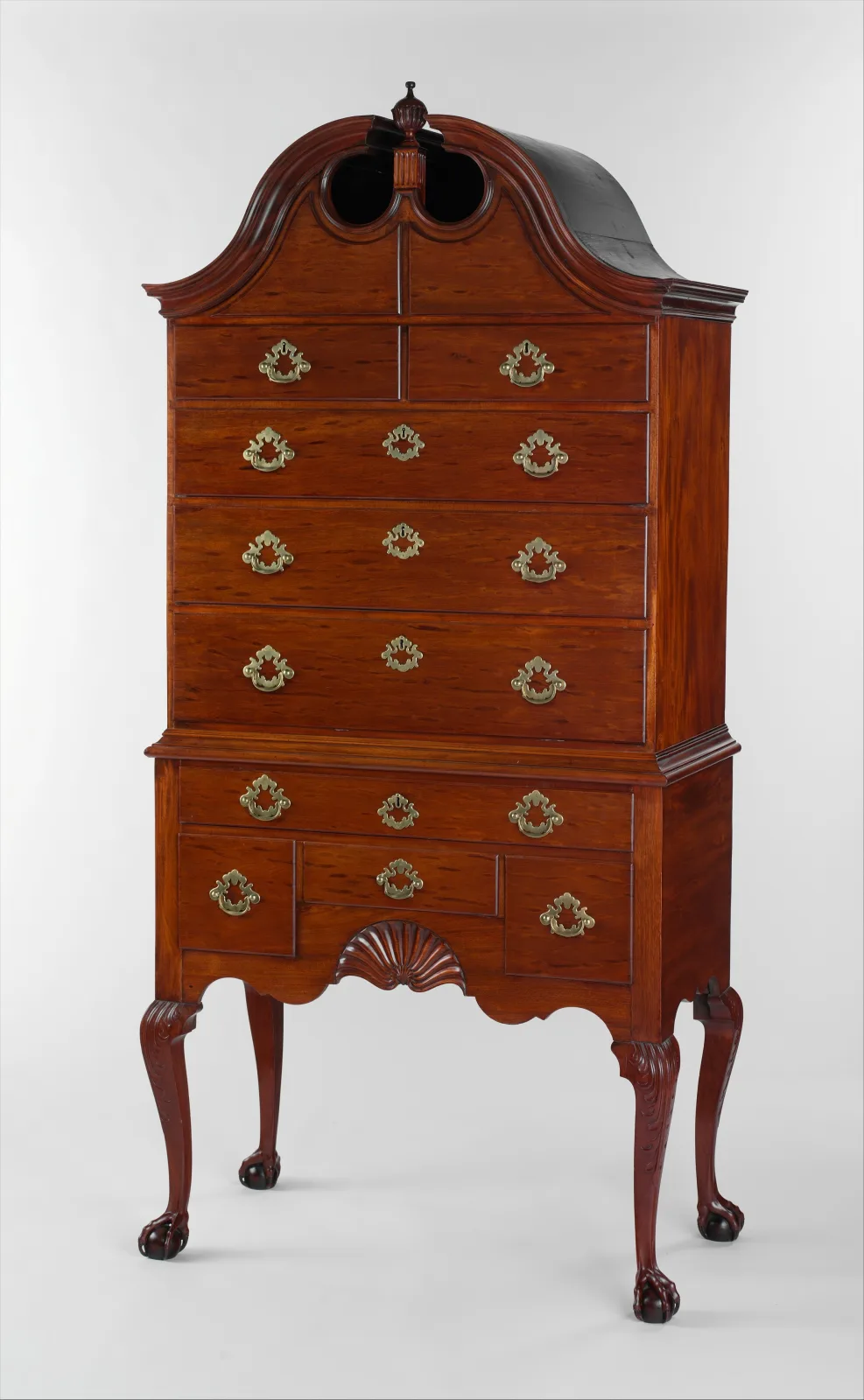 A tall mahogany high chest of drawers with a scrolled bonnet top, an upper case of drawers resting on a lower case with a carved shell and cabriole legs