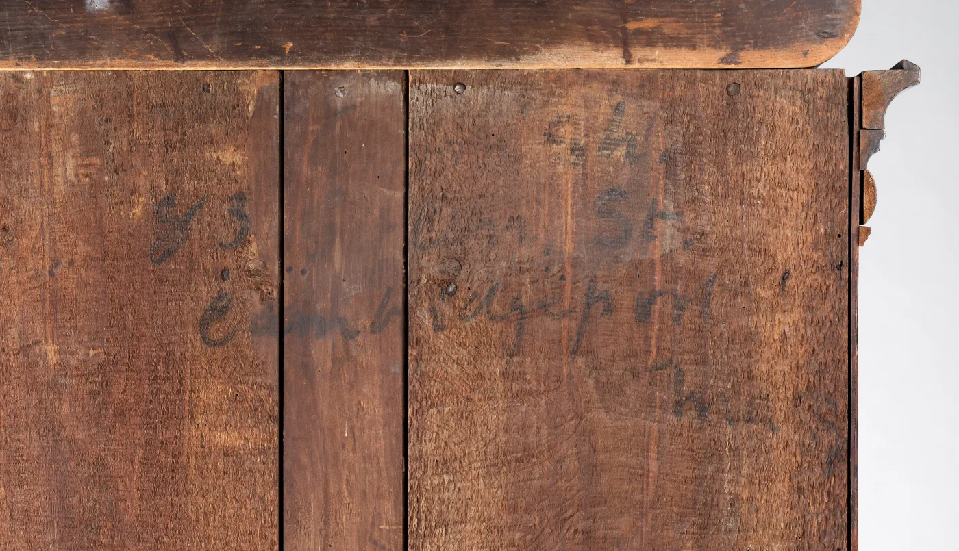 Close view of unfinished vertical backboards on a high chest, with a handwritten inscription in dark ink running across two of the boards