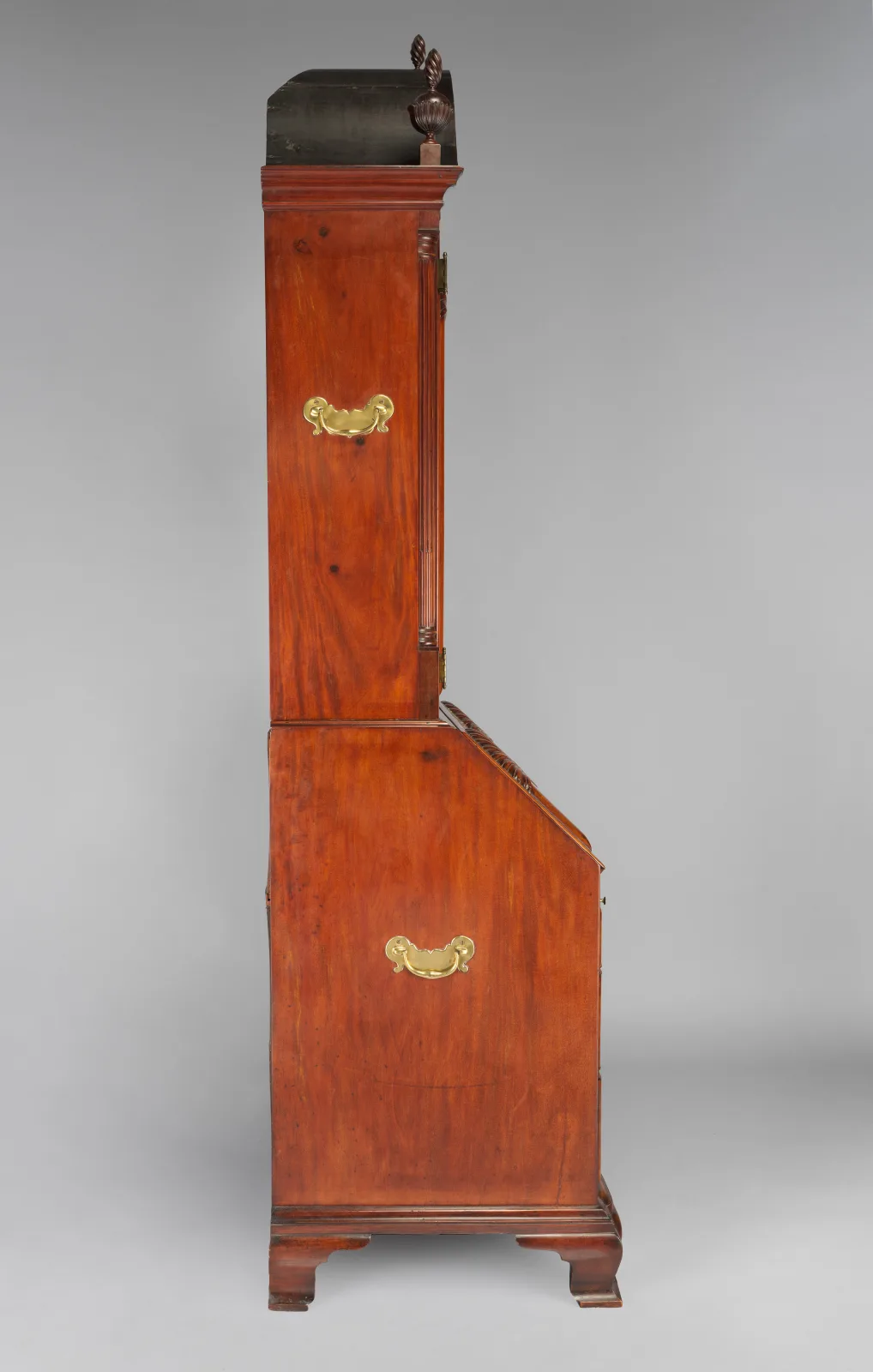 Side view of a tall mahogany desk and bookcase, with the shallower bookcase section sitting on the deeper slant-front desk below it
