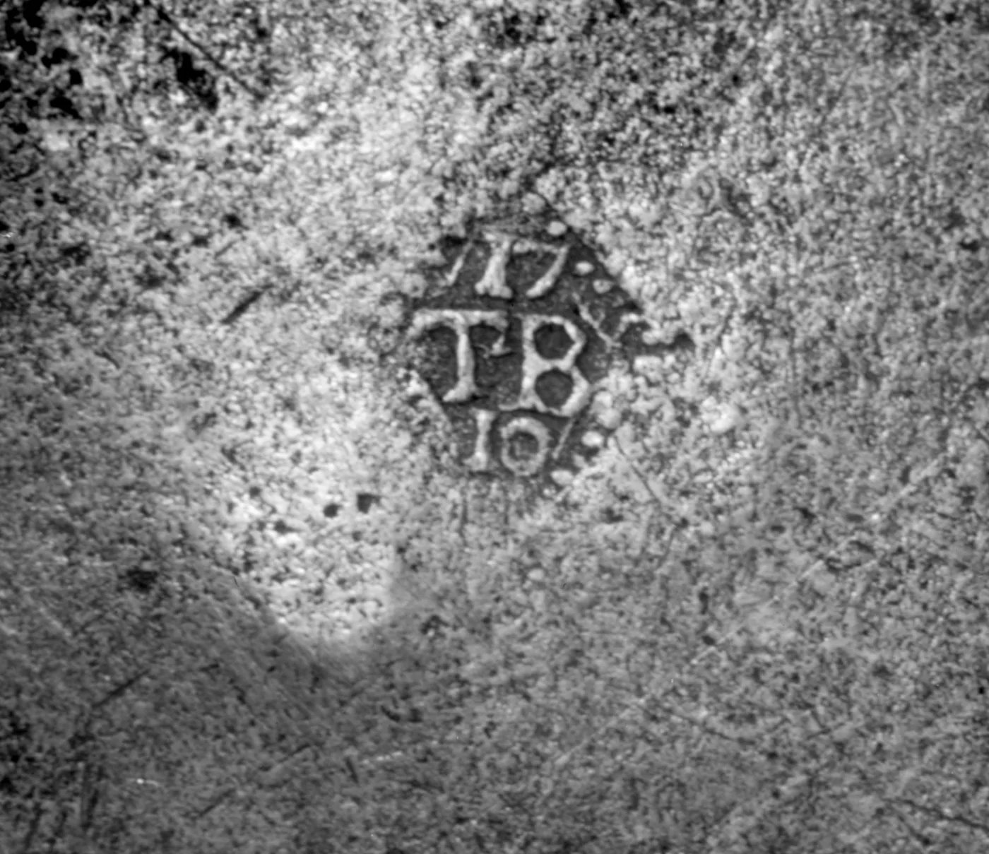 Close view of a small lozenge-shaped mark struck into grey pewter, reading 17 above, TB in the centre and 10 below