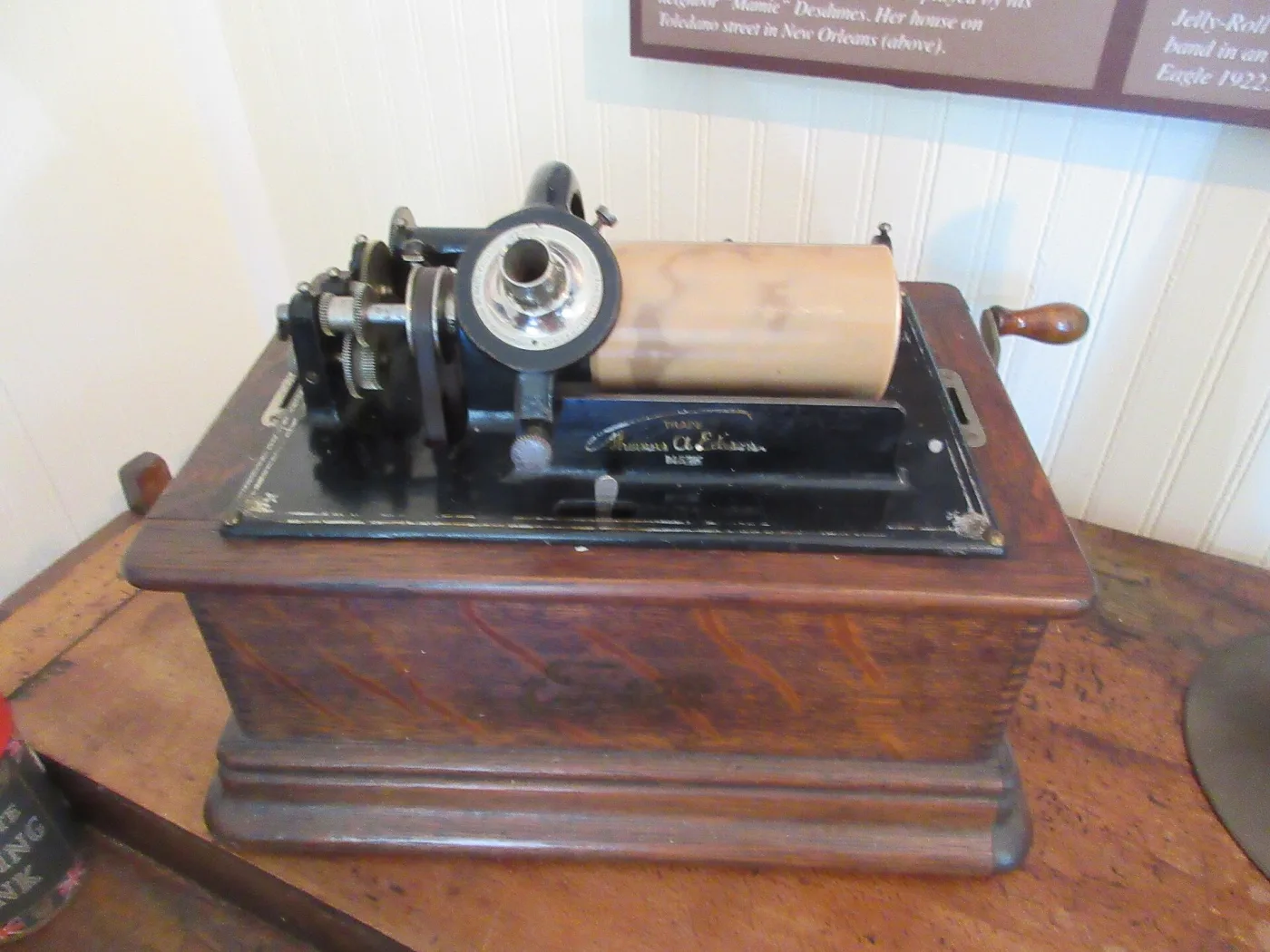 Edison cylinder phonograph in an oak case with a wax cylinder on its mandrel, a nickelled reproducer arm above it and a large flaring metal horn beside it on a table