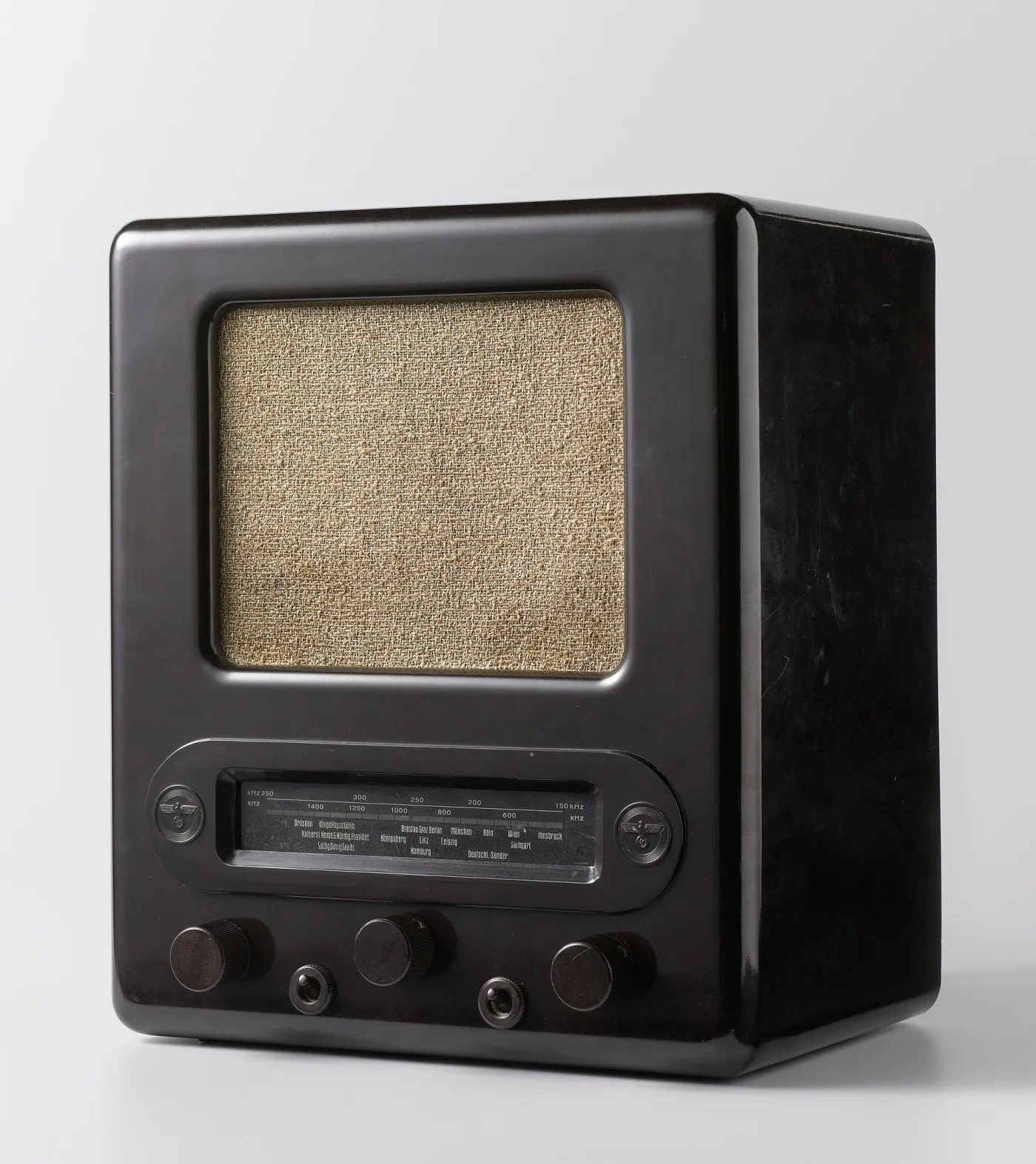 Small dark brown moulded radio cabinet with a rounded top, a circular fabric-covered speaker opening filling most of the front and two control knobs at the bottom