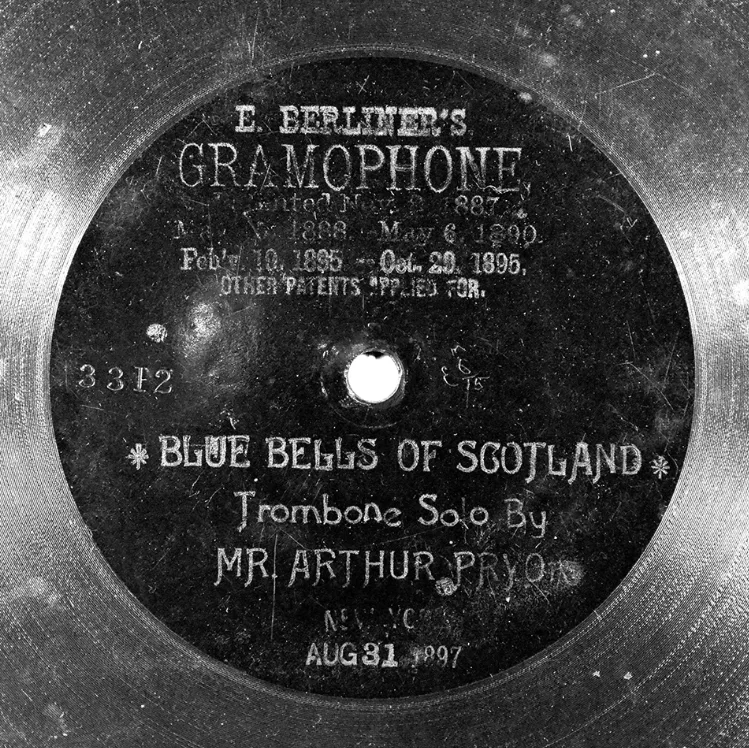 Early gramophone disc photographed face on, its centre area etched with the words E. Berliner's Gramophone, Blue Bells of Scotland, Trombone Solo by Mr Arthur Pryor, and a date
