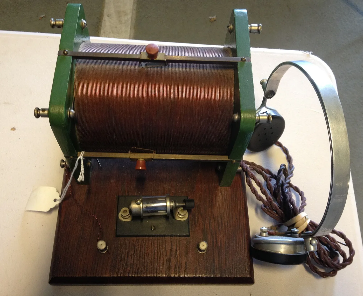 Crystal radio set built on a wooden base, with a large cylindrical coil wound on a green former, a small crystal detector, a variable capacitor and a pair of headphones with a metal band