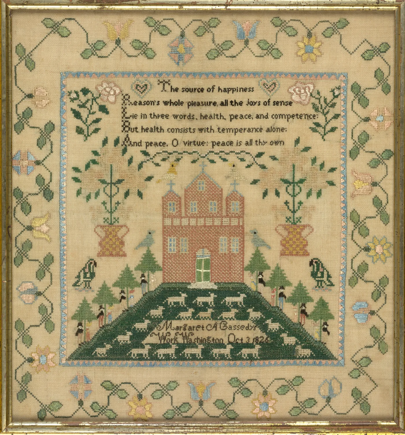 Square silk sampler with a verse panel at the top, a brick house with three gables on a green mound below it, and a flowering vine border