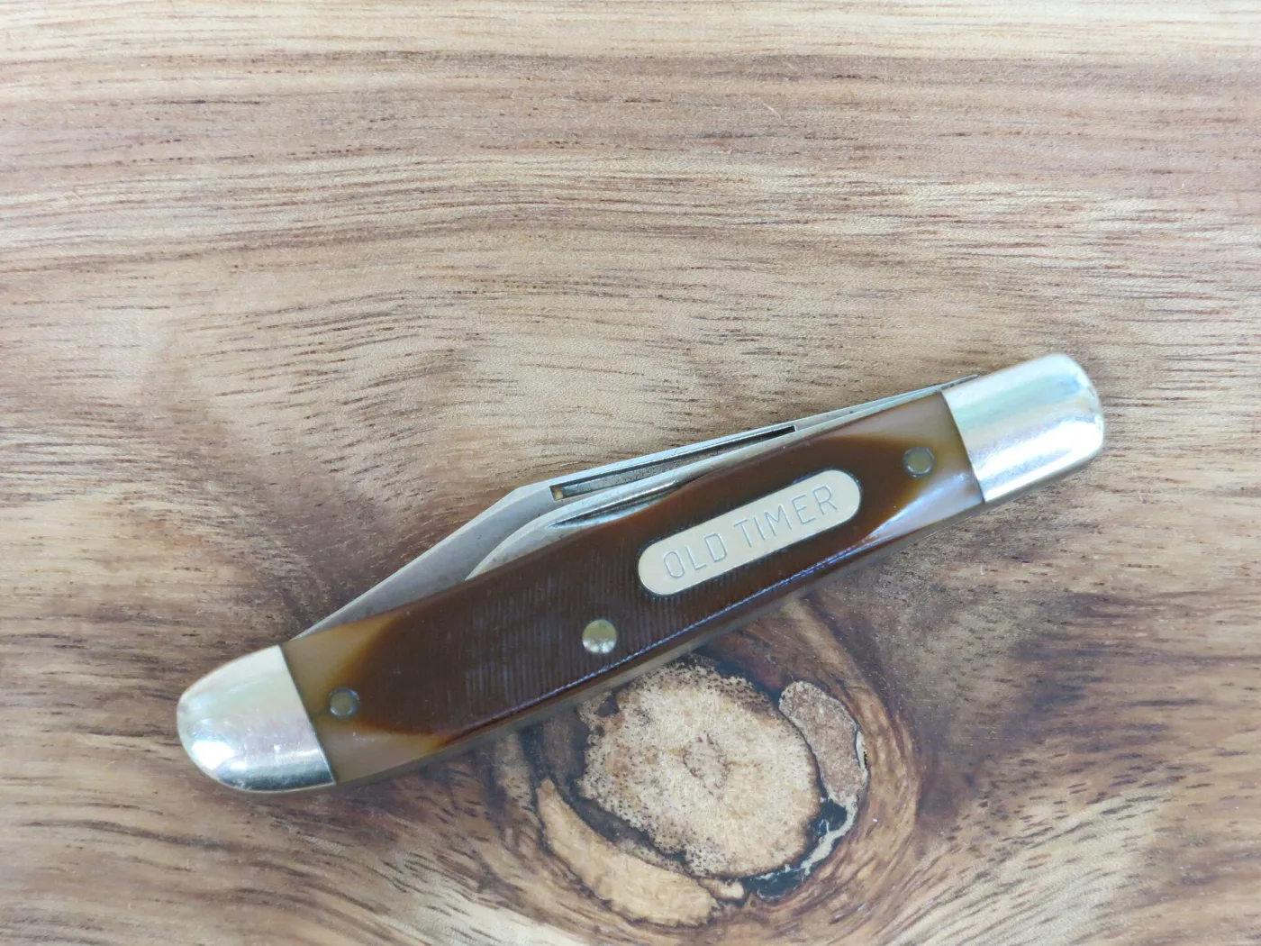 A closed Old Timer stockman lying on wood, showing brown sawcut handles, a white OLD TIMER shield and nickel silver bolsters