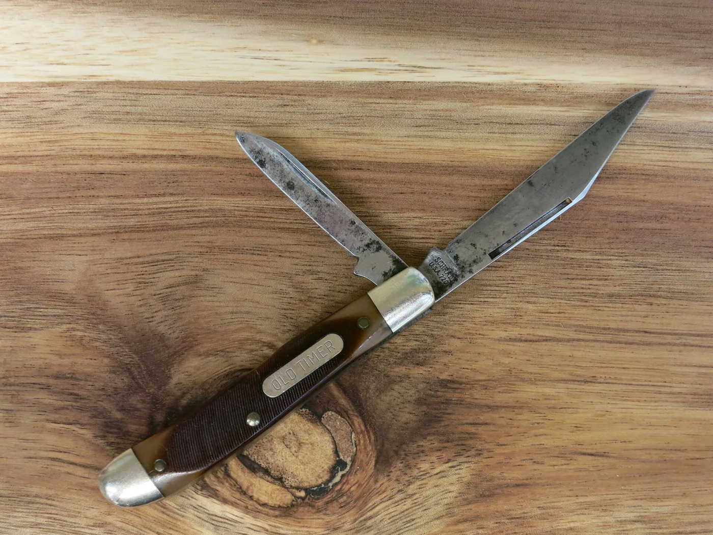 An Old Timer stockman with its clip and spey blades open, the blades heavily darkened with patina, resting on wood