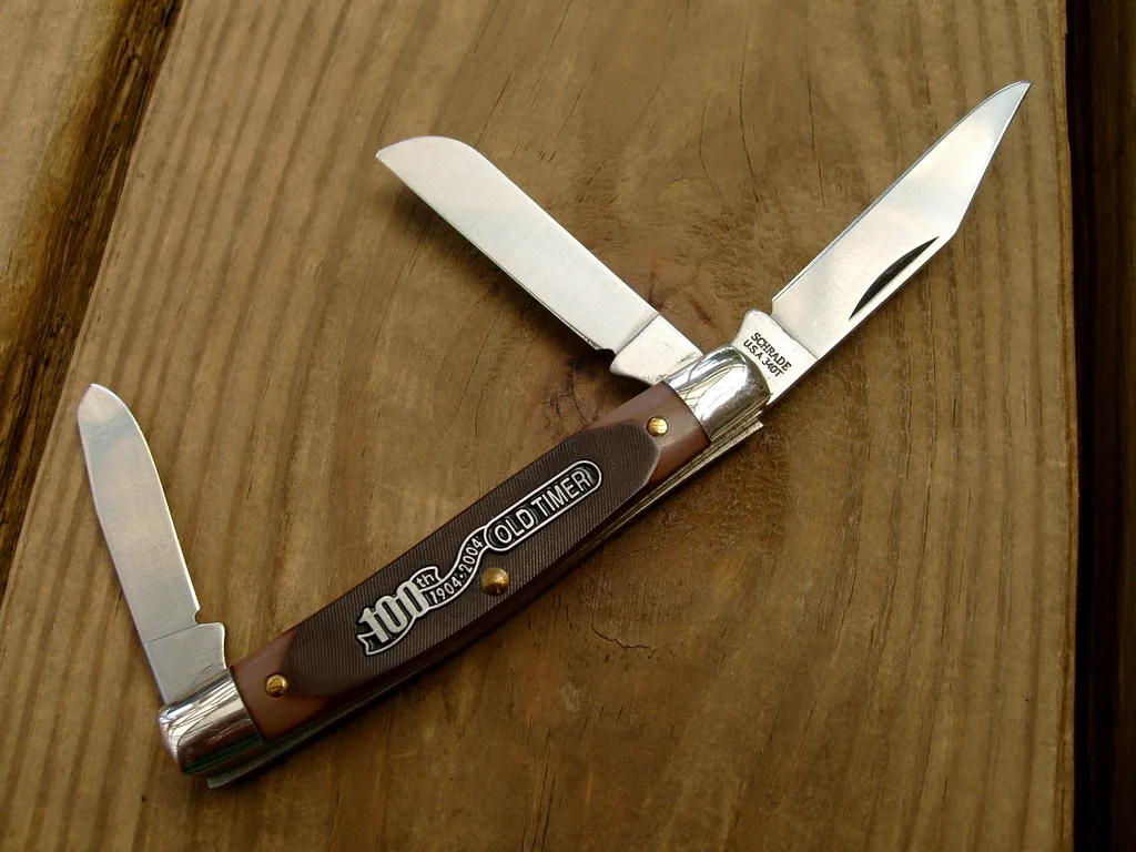 An Old Timer three-blade stockman with blades open on a wooden table and a shield reading 100th 1904-2004 Old Timer on the brown sawcut handle