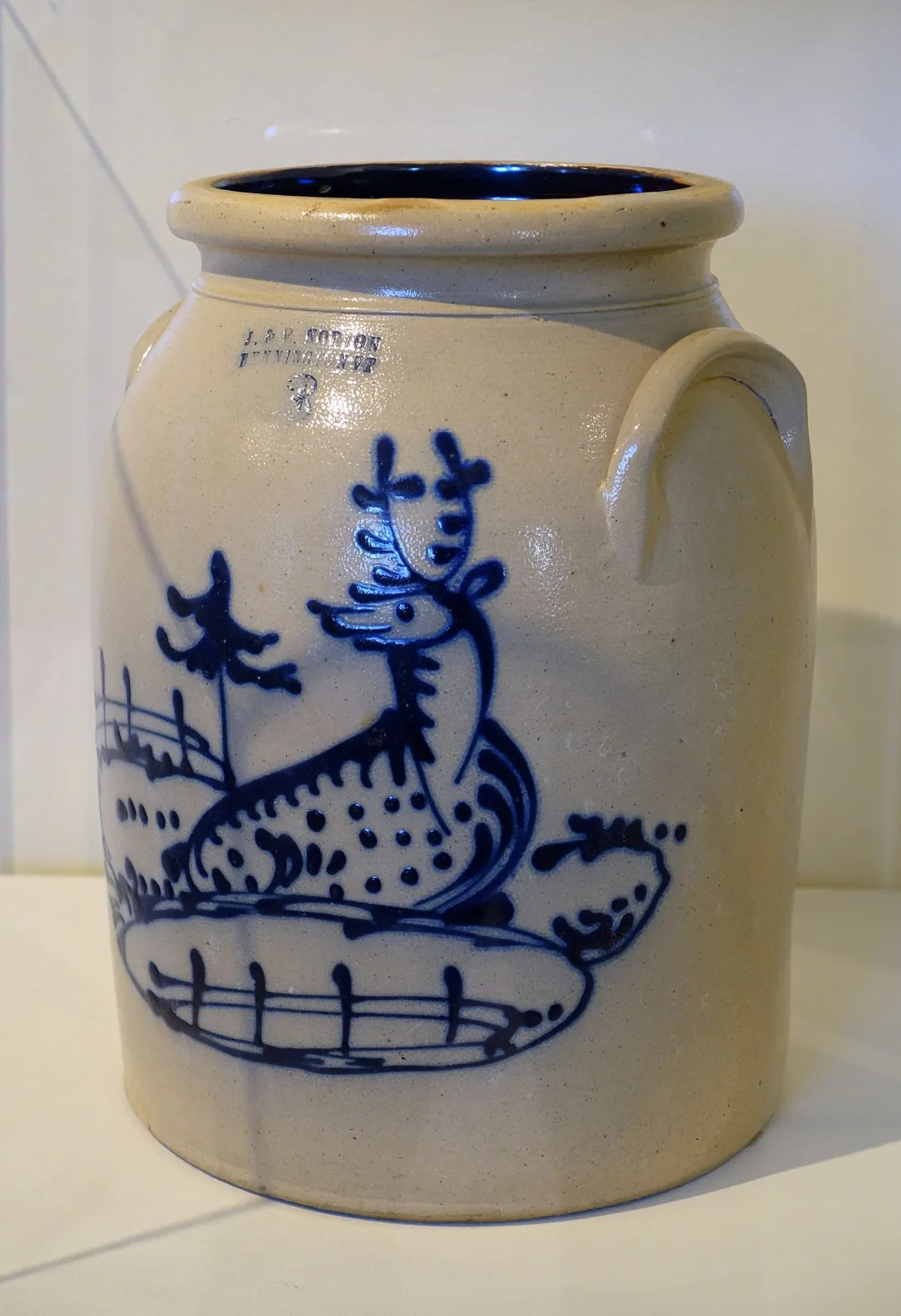 Grey salt-glazed stoneware jar with an impressed maker's mark and capacity numeral near the rim, decorated in cobalt blue with a spotted deer standing before a fence and a pine tree, and a dark glazed interior visible at the mouth