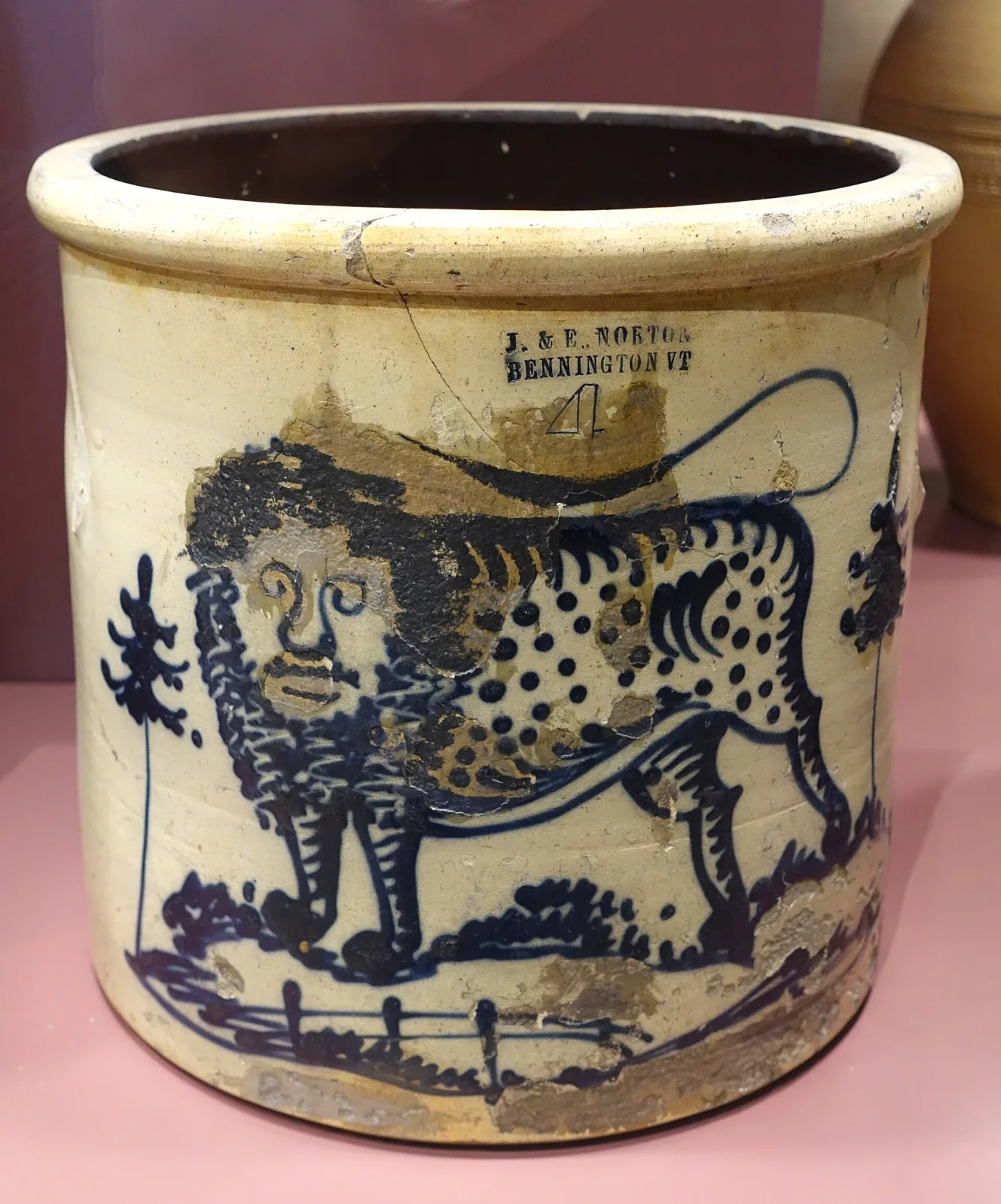 Four-gallon grey stoneware crock decorated in cobalt with a large maned lion with a spotted body standing in a fenced landscape, with an impressed maker's mark and a hand-drawn numeral 4, and areas where the cobalt and glaze have flaked away to bare buff clay