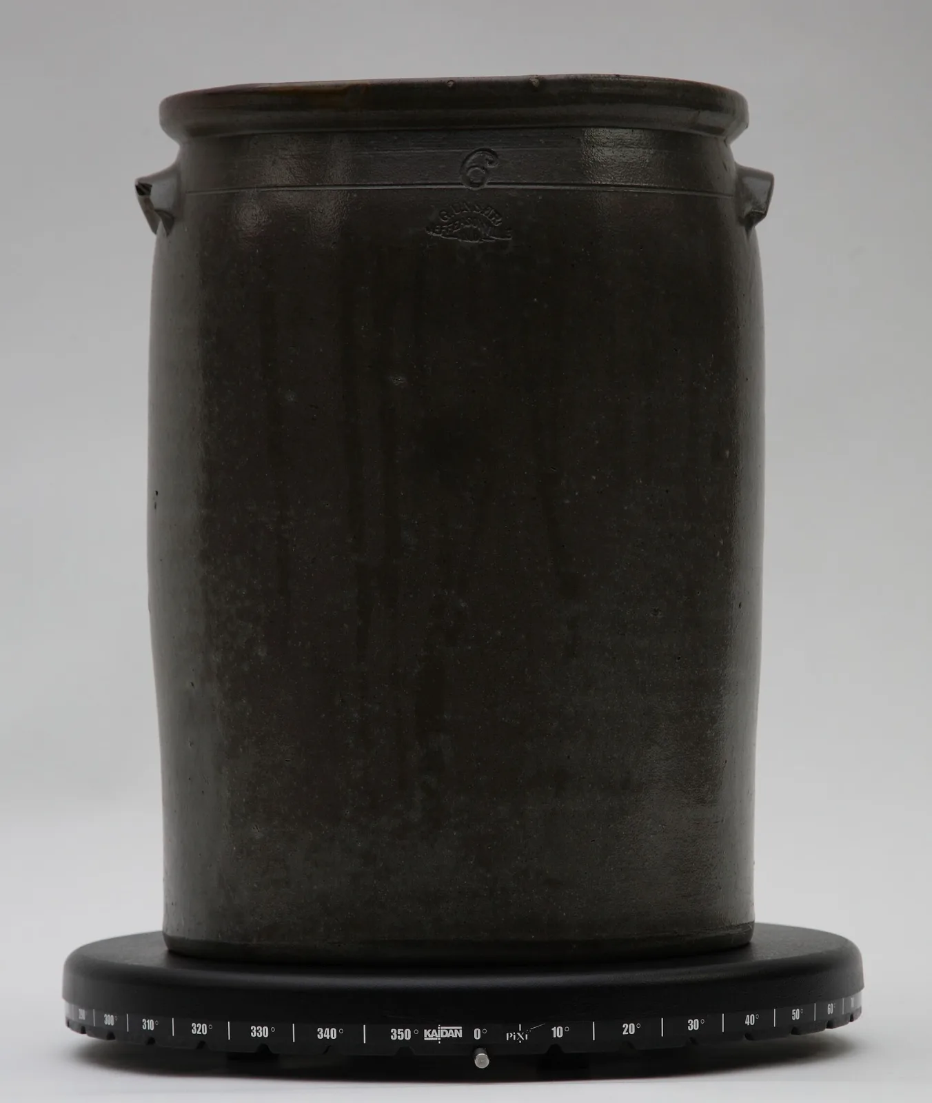 Cylindrical stoneware jar covered inside and out in a glossy dark brown slip glaze, with lug handles, an impressed numeral 6 and an arched impressed maker's die