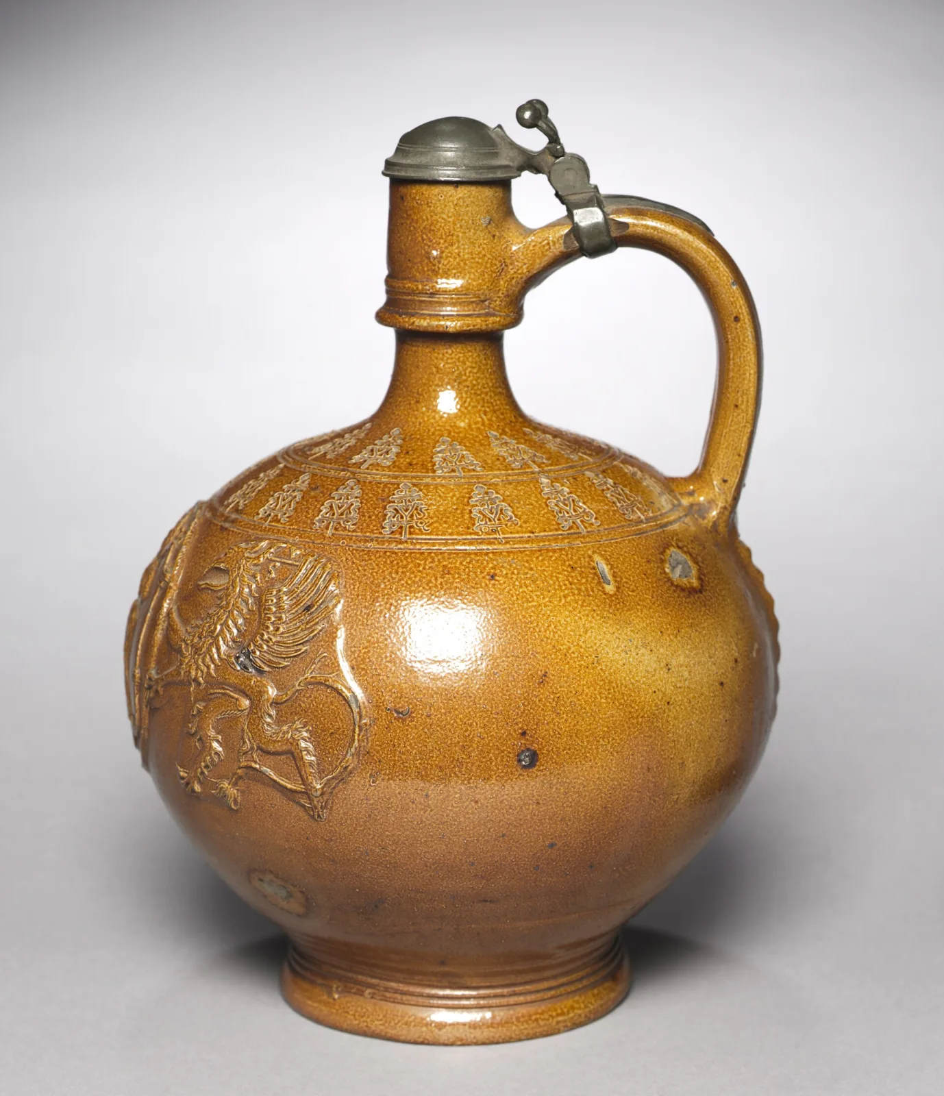 Globular tan-brown salt-glazed stoneware jug on a turned foot ring, with a loop handle, a hinged pewter lid with thumb-lift, a band of stamped repeating motifs around the shoulder and an applied moulded relief medallion of a rampant winged beast