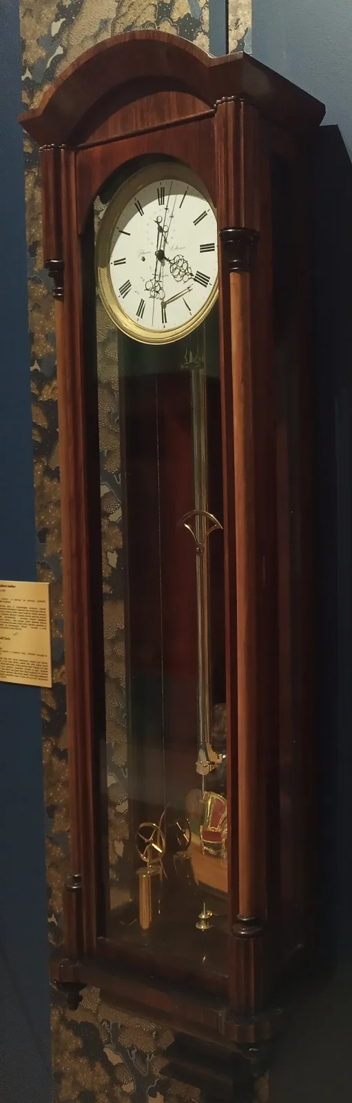 Dark rosewood wall regulator with an arched cornice, slender turned columns either side of a long glass door, a white dial with a central seconds hand and a brass pendulum