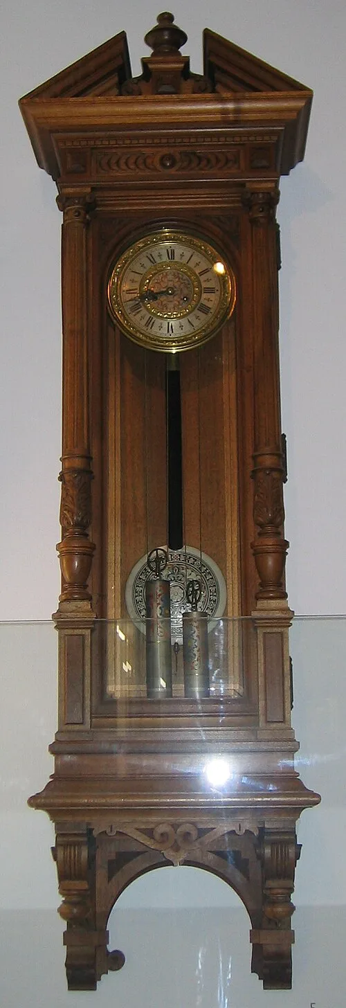 Tall carved walnut regulator in a museum case, with a broken pediment and urn finial, carved brackets, turned half-columns, a brass dial, two weights and an arched open base