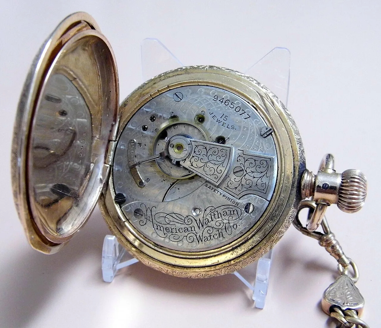 Open hunting-case pocket watch showing a nickel movement engraved with the serial number 9465077, 15 Jewels and American Waltham Watch Co. in script
